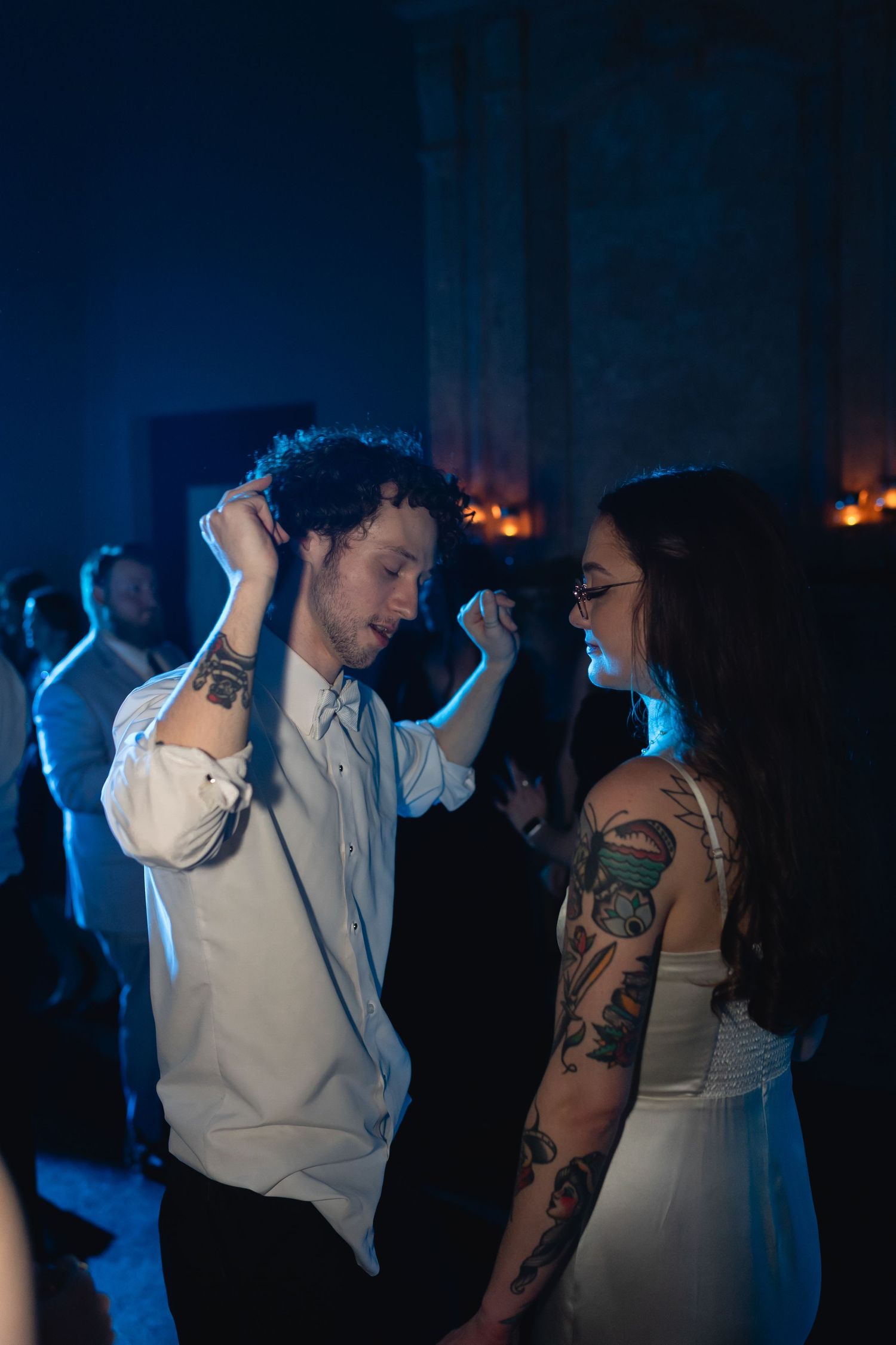Two people dancing together at a nightclub with moody blue lighting and tattoos visible in a candid moment.