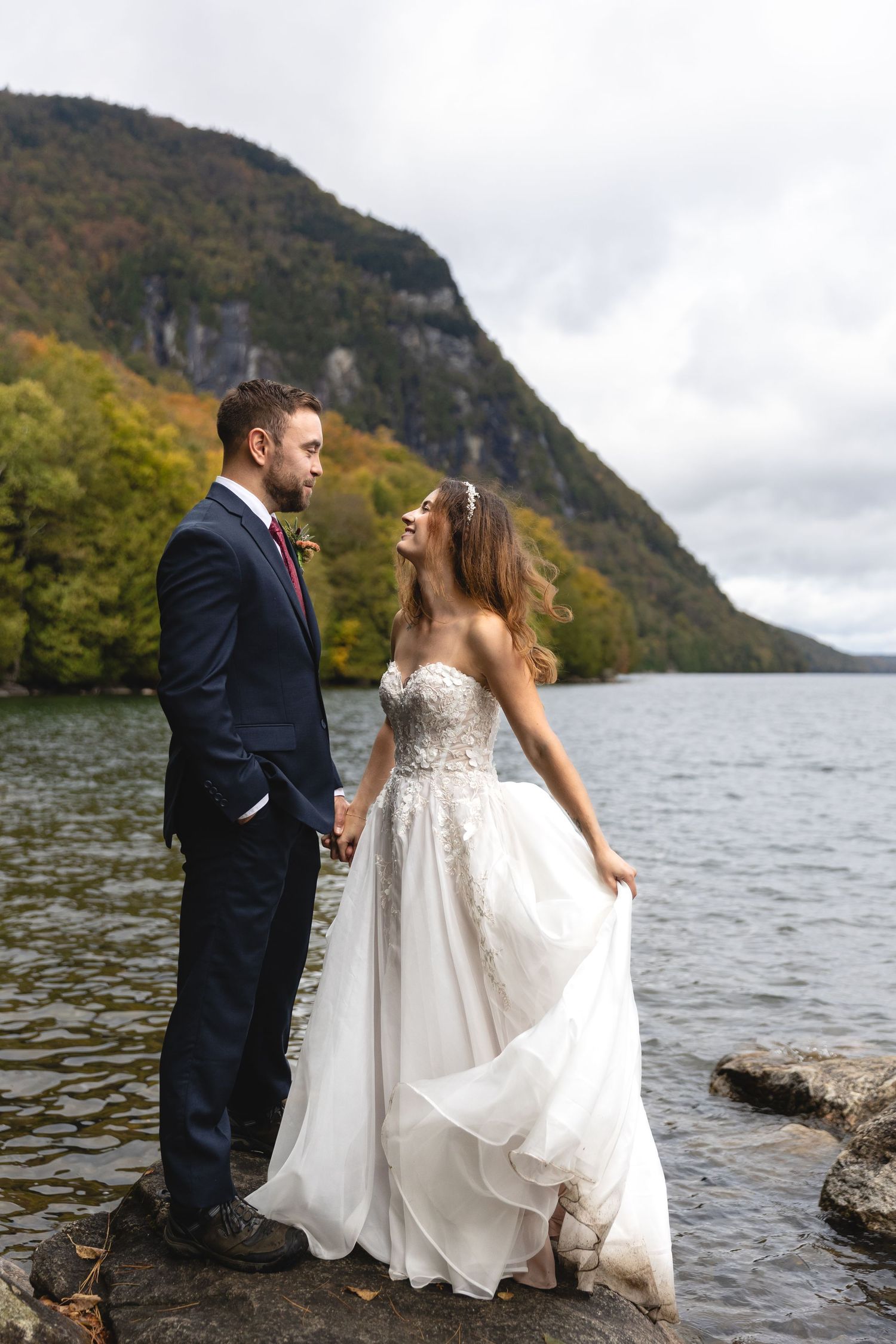 Couple standing by lakeside with mountain backdrop in autumn.