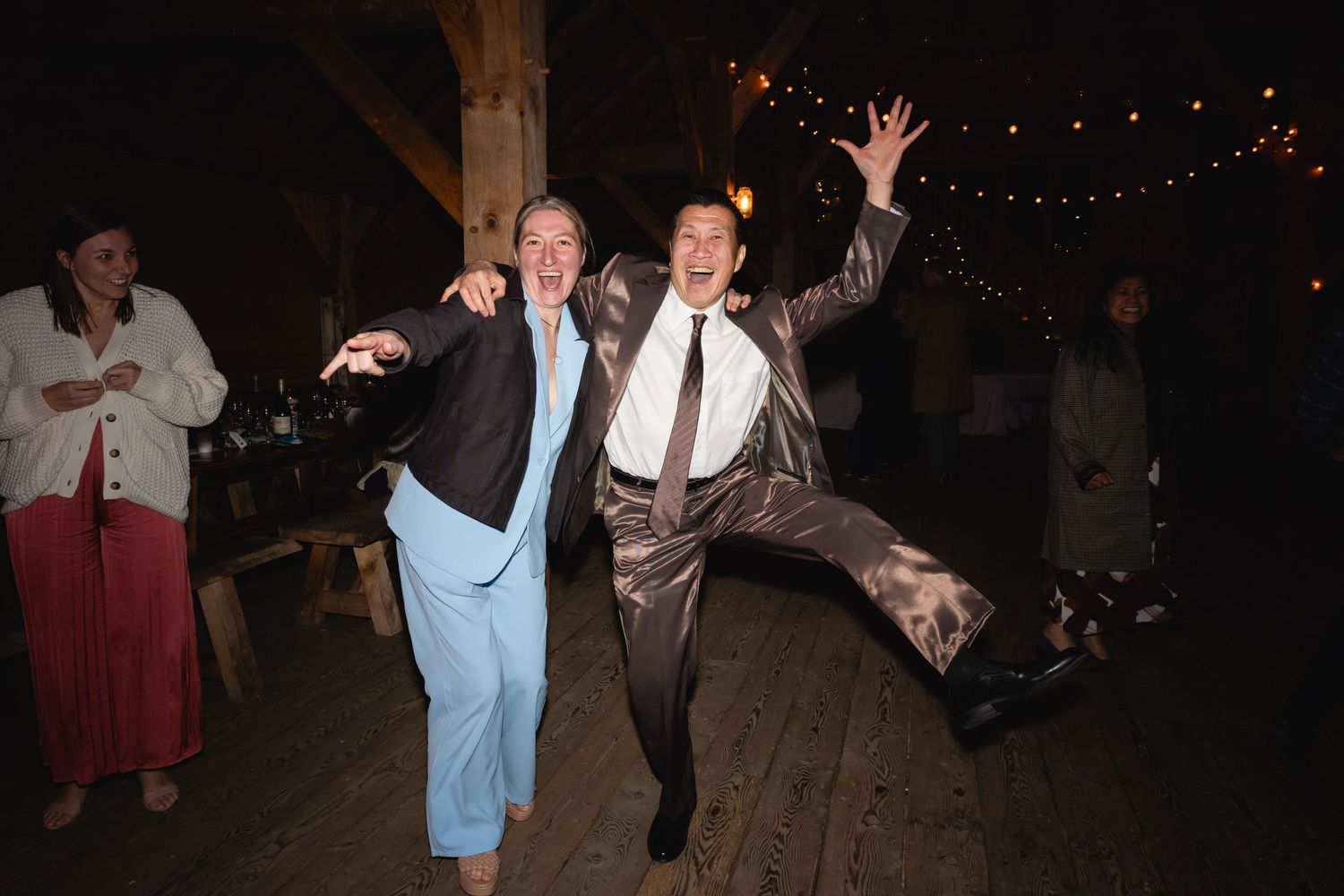 Two people dancing energetically at a nighttime party with string lights visible in the background.