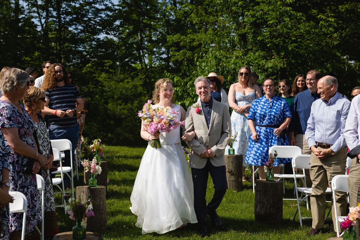 Outdoor wedding ceremony takes place in a lush garden setting with guests seated in white chairs.