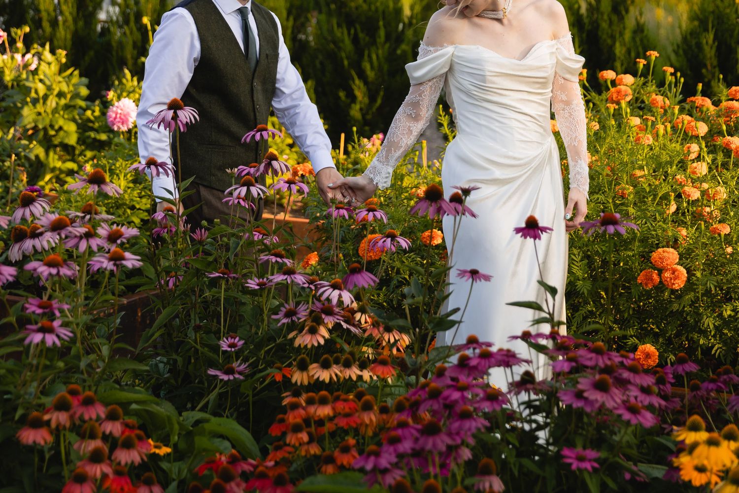 A couple poses together in a vibrant garden filled with orange and purple coneflowers on their wedding day.