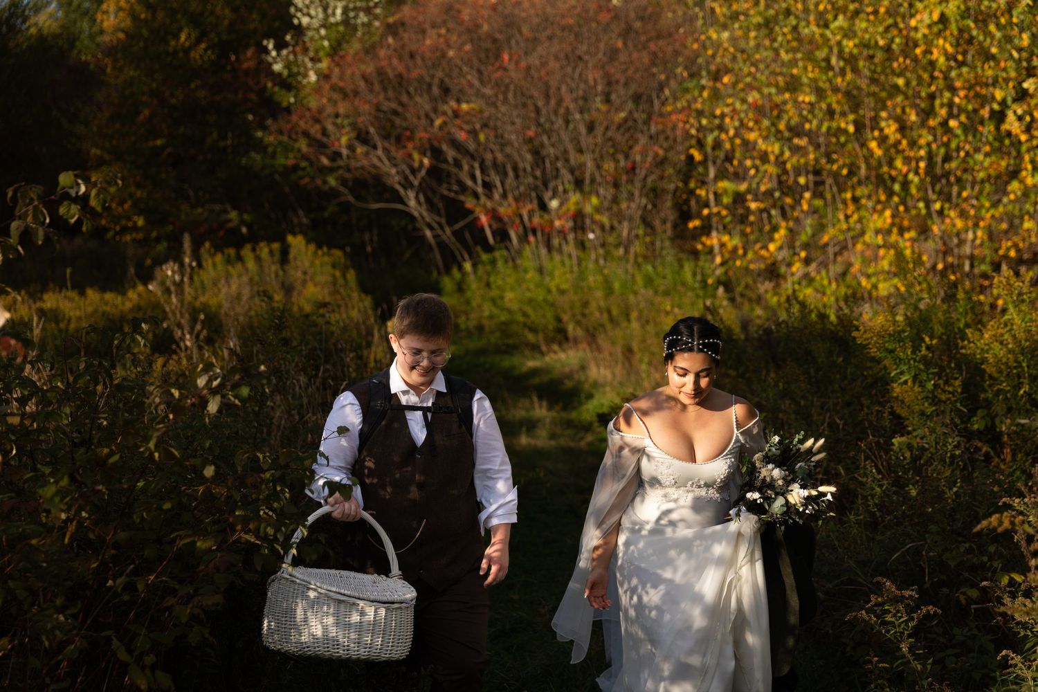 A couple strolls through a garden with autumn foliage in the background.