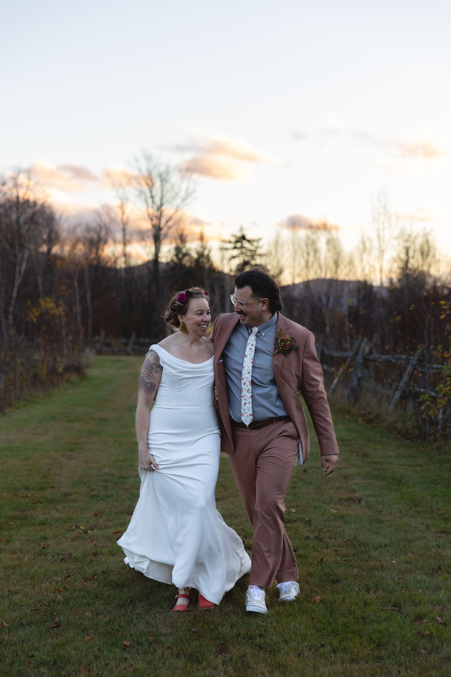 Wedding couple walks together on a grassy path at sunset.