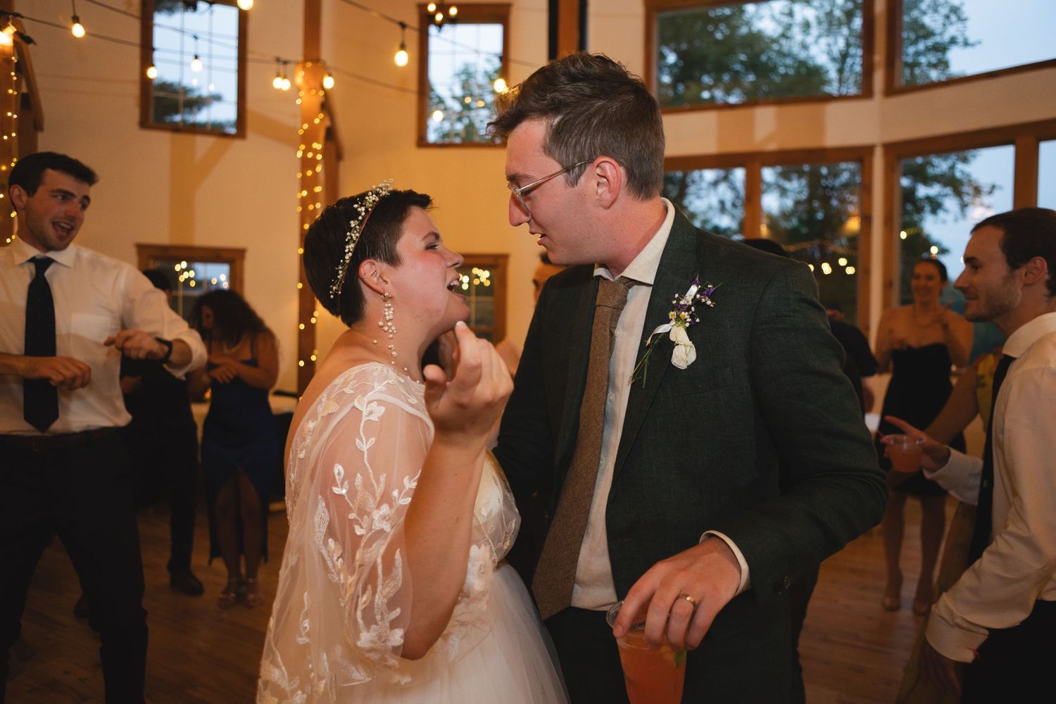 Joyful moment during a wedding reception dance under warm lighting and string lights.