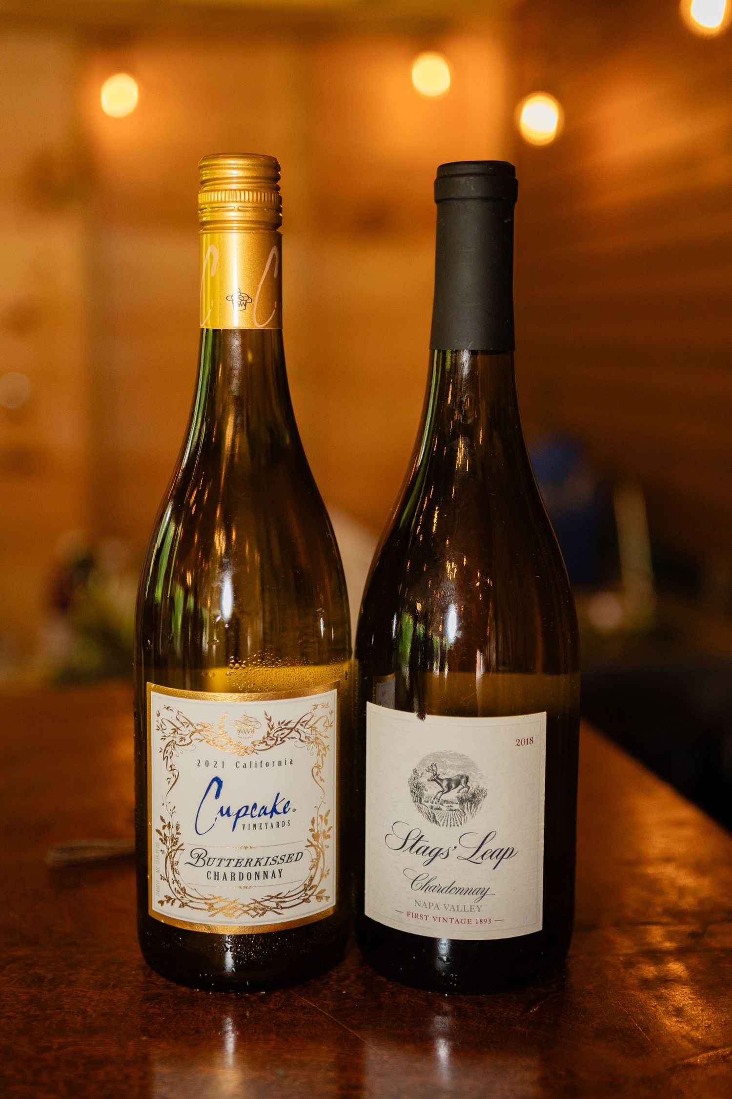 Two bottles of white wine displayed on wooden surface with warm ambient lighting.