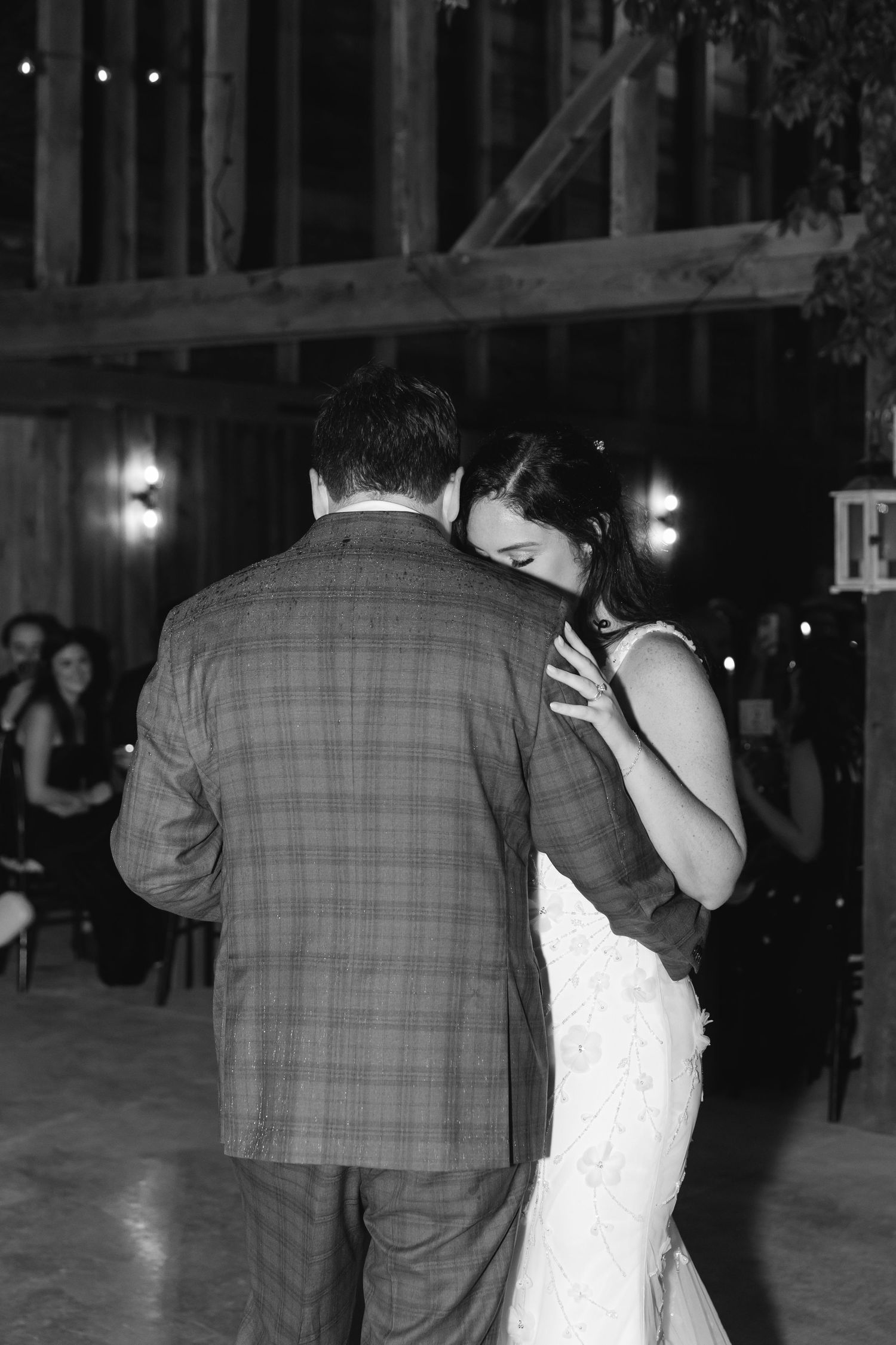 A couple shares an intimate dance at a wedding reception in a rustic barn venue lit by soft glowing lights.