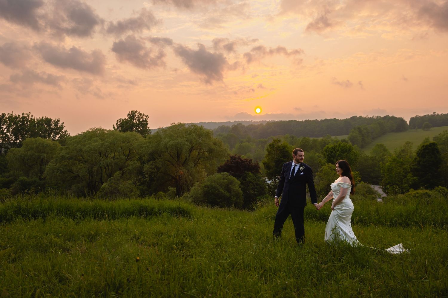 A couple walks together on a lawn beside a white farmhouse on a sunny afternoon.