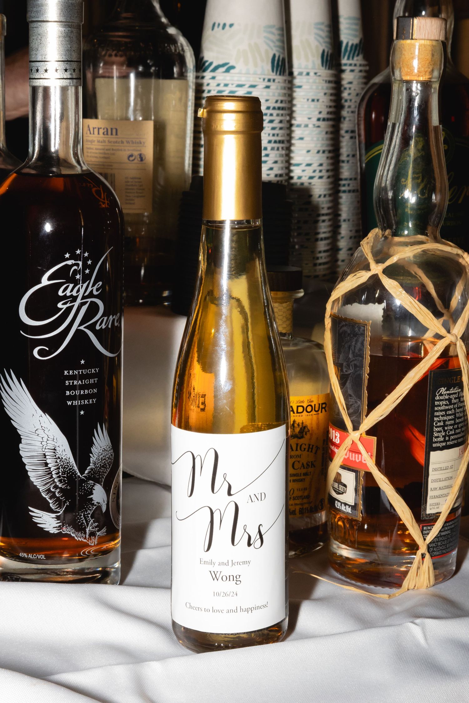 Bottles of premium liquor including Eagle Rare bourbon and a gold-labeled wine bottle arranged on white cloth.