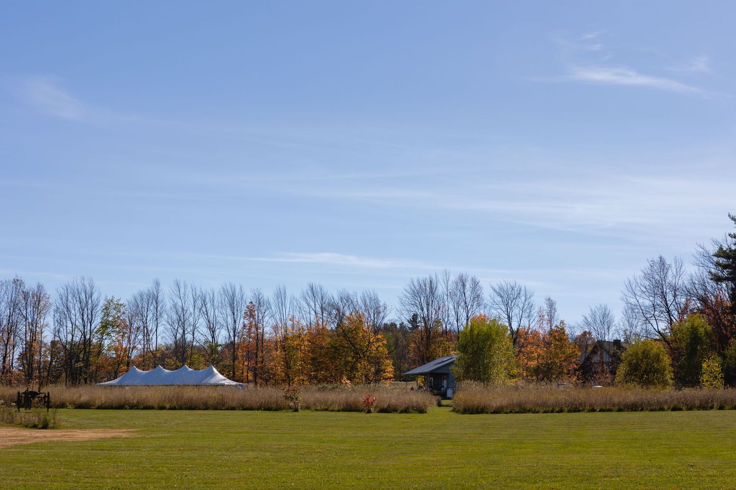 Panoramic view of a rural landscape with autumn trees and farm buildings nestled against a clear blue sky.