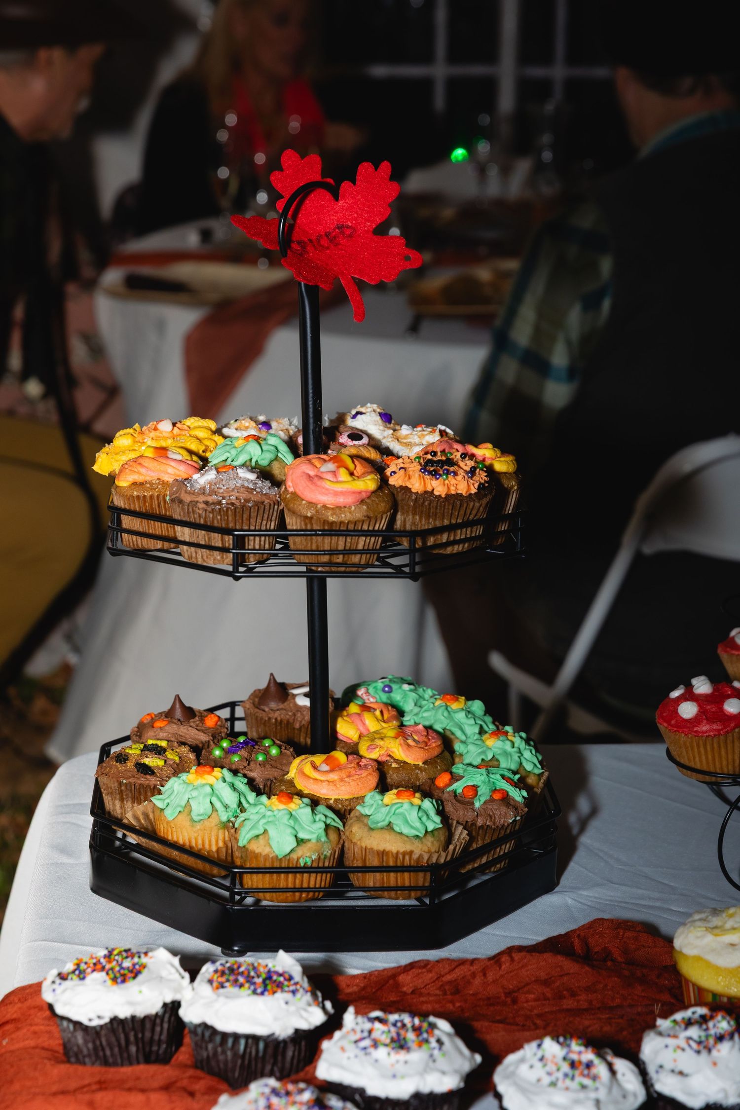 Tiered display of colorful cupcakes decorated with frosting flowers and sprinkles at a dessert table.