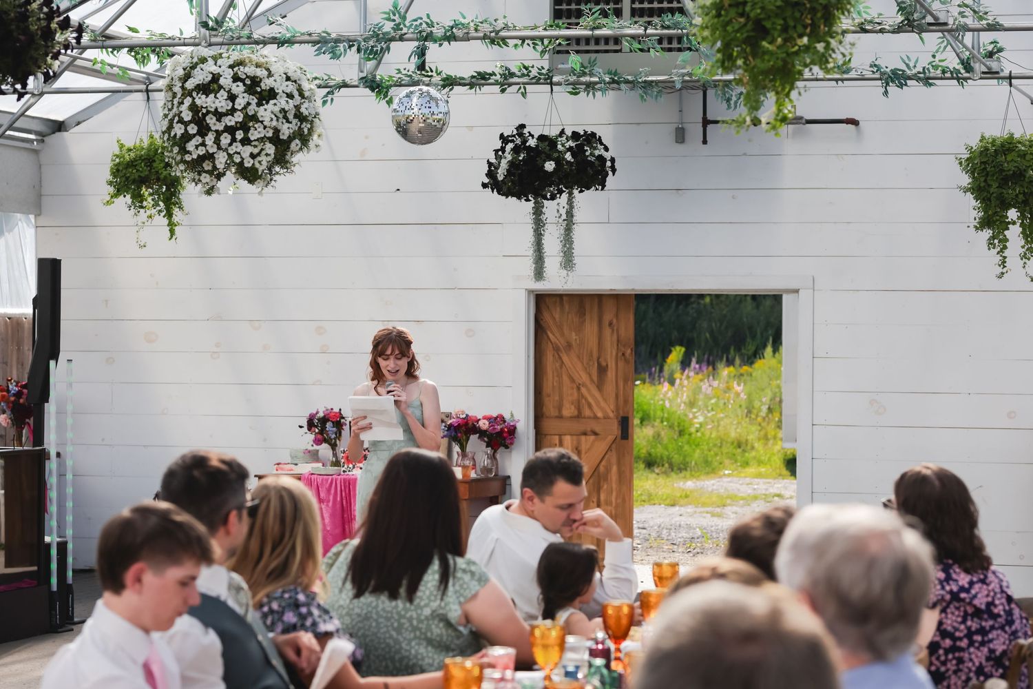 Wedding guests gather at rustic outdoor reception tables decorated with floral centerpieces and string lights.