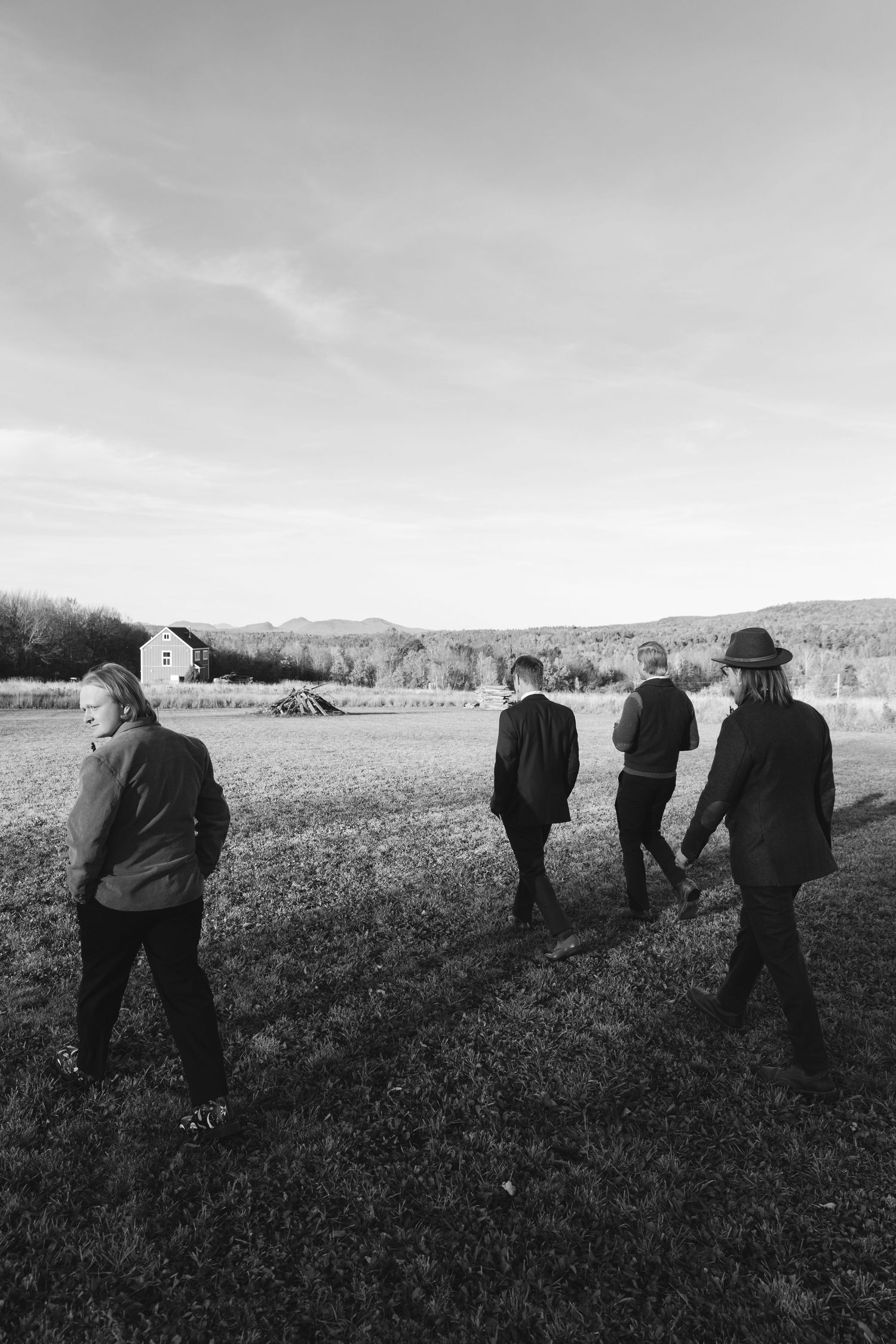 Several figures in dark clothing stand scattered across a vast open field on an overcast day.
