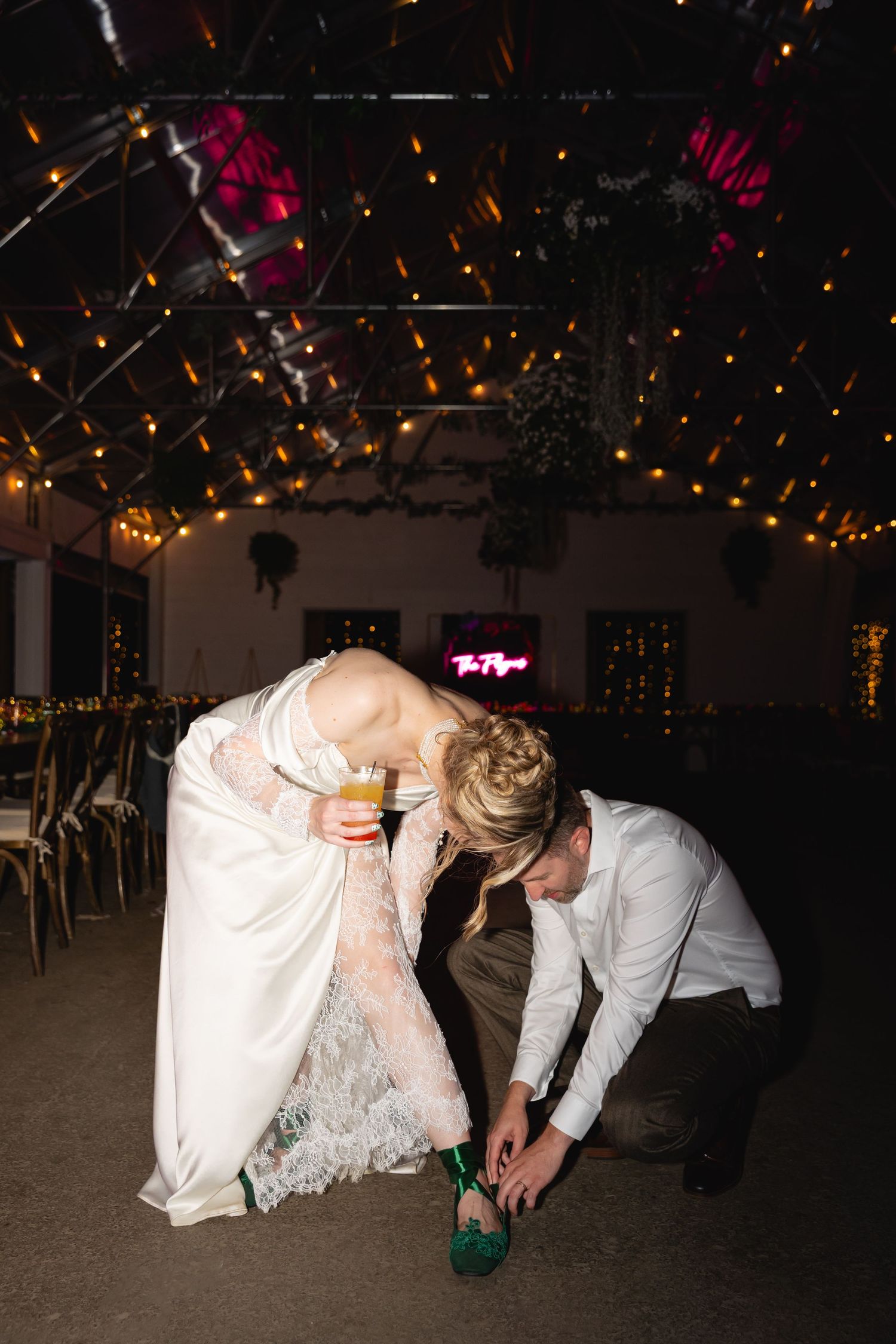 Wedding couple bends down to perform a synchronized dance move under twinkling lights at their reception.