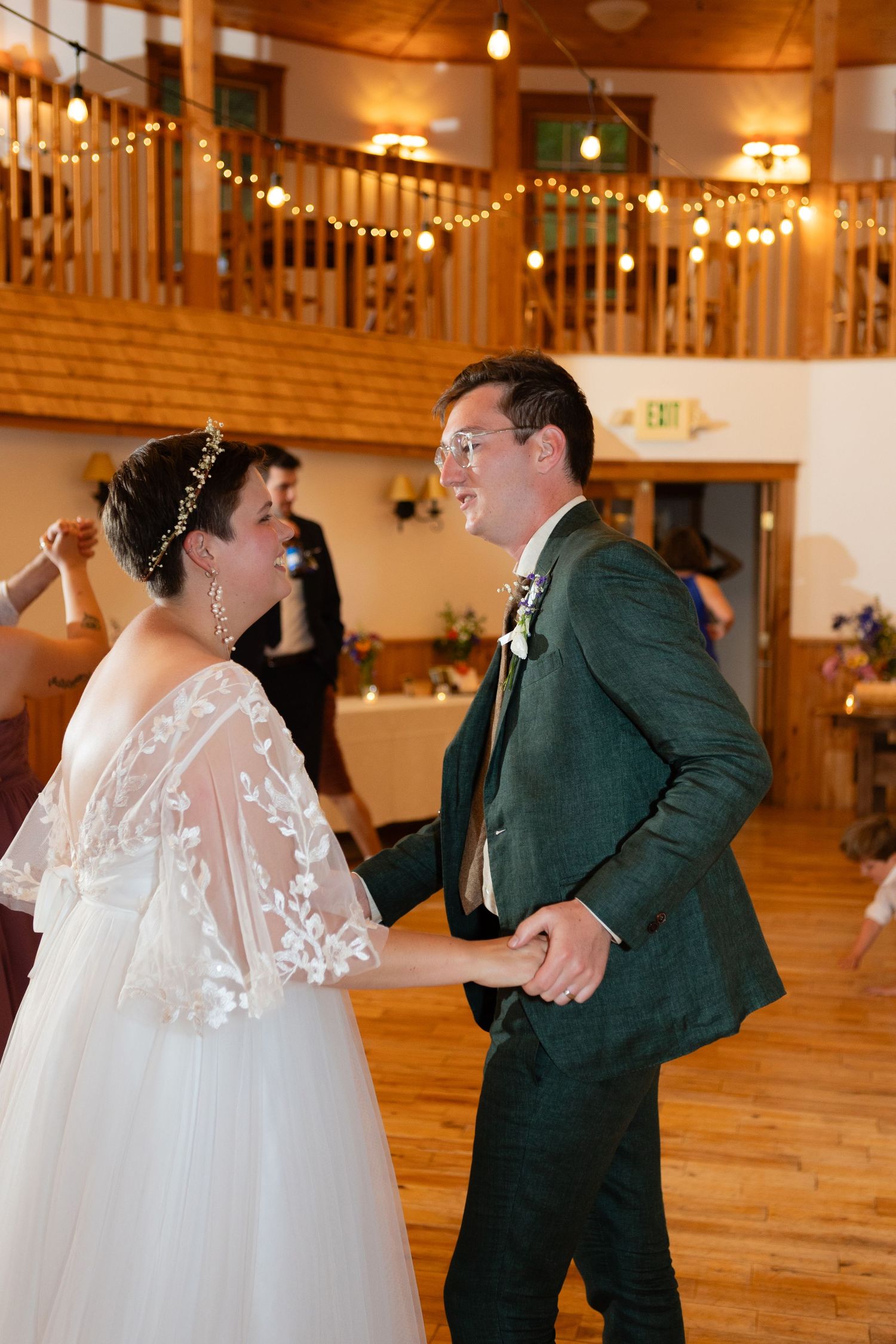 Newlyweds dancing in a rustic venue decorated with string lights and wooden balcony.
