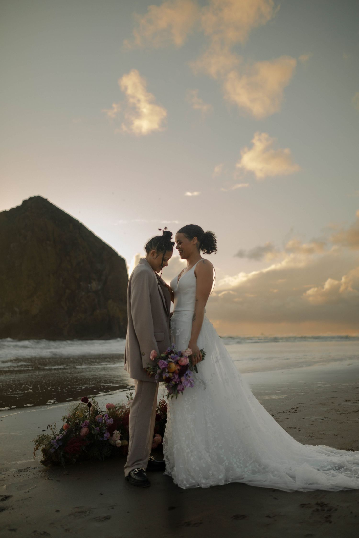 A romantic wedding couple embraces on a beach at sunset with Haystack Rock silhouetted in the background at Cannon Beach.