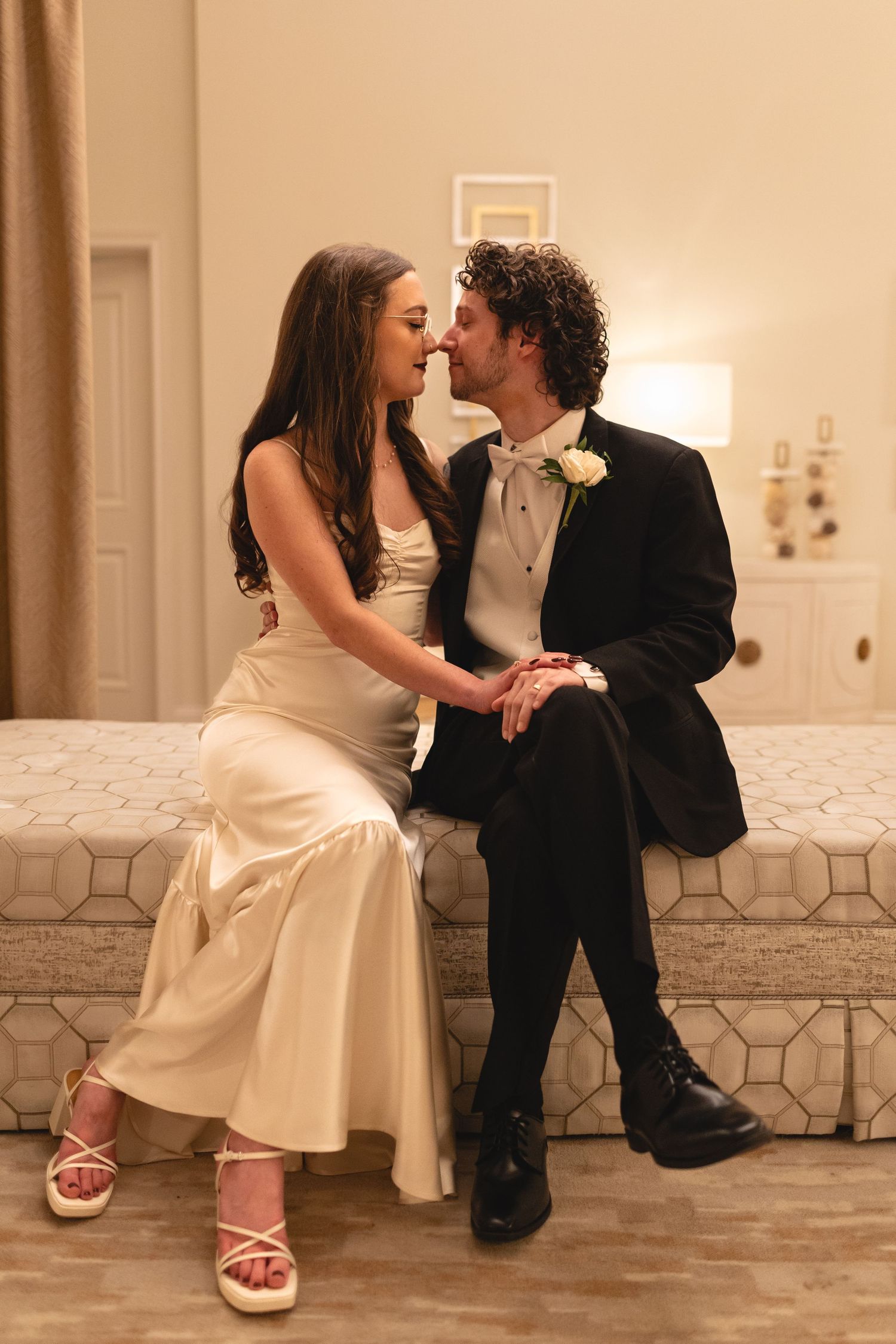A couple shares an intimate moment on their wedding day wearing formal attire and sitting together on a bench.
