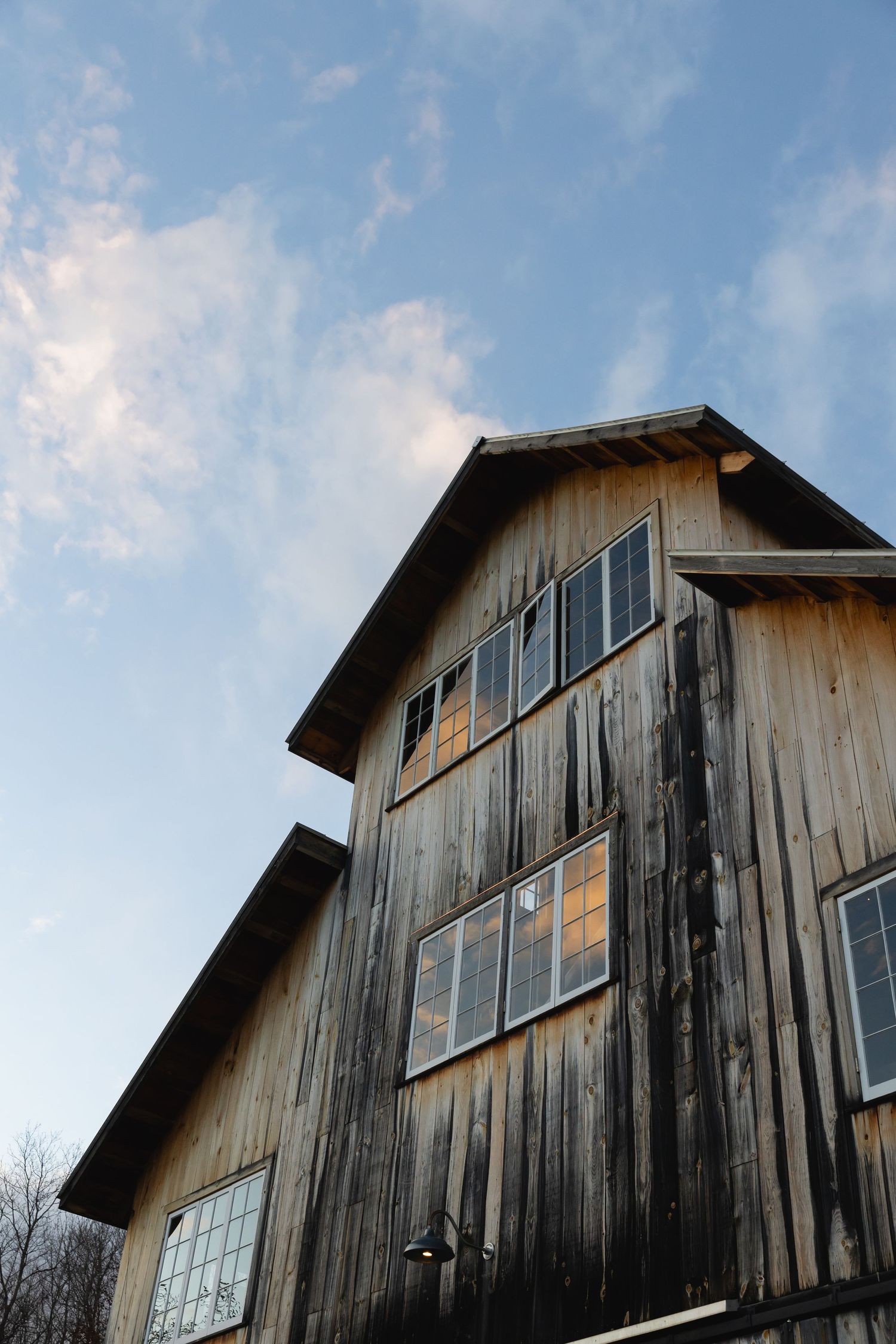 Old weathered wooden barn with windows reflects golden sunlight against a blue sky with wispy clouds.