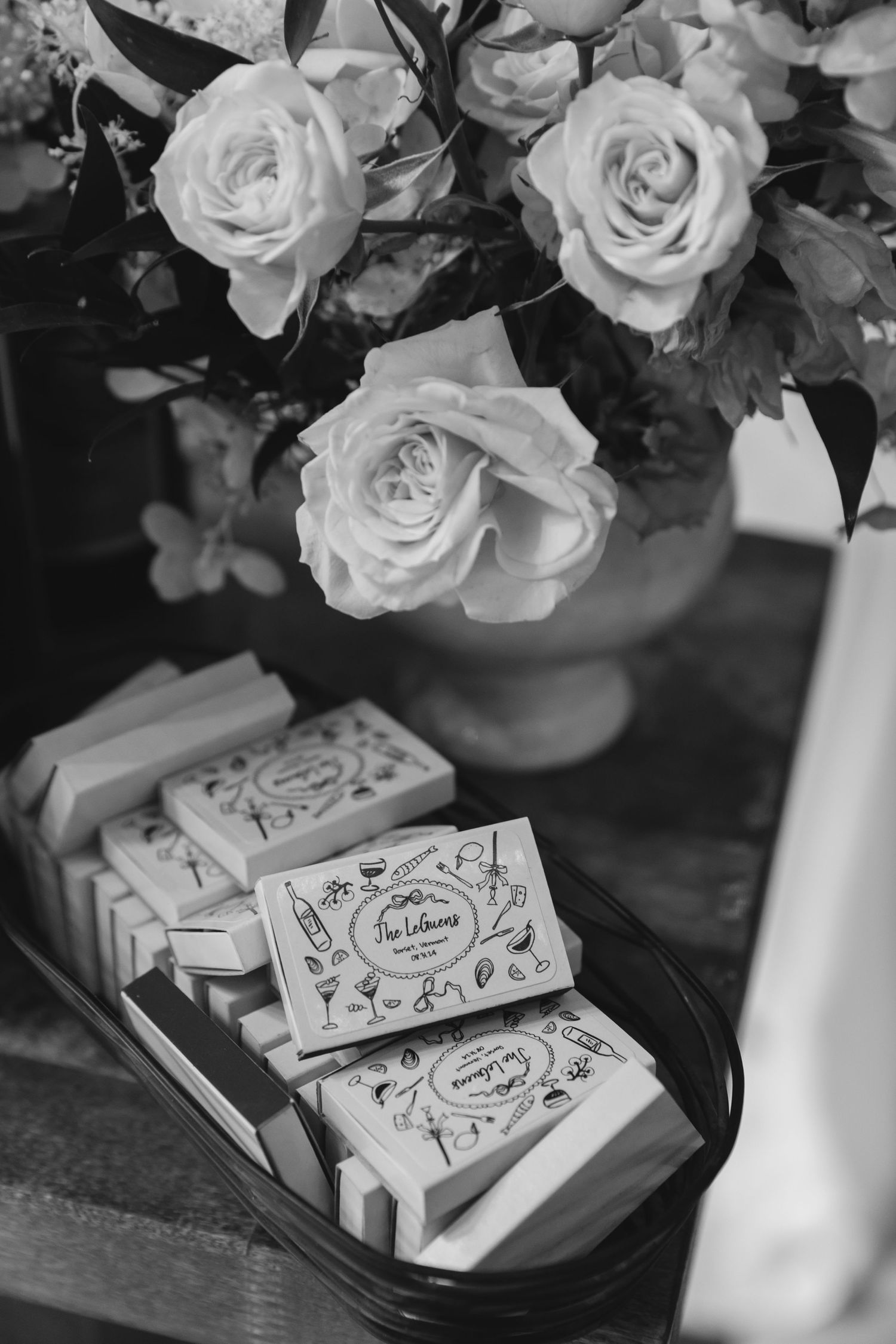 Black and white photograph of roses in a vase with decorative soap bars displayed below in a rustic setting.