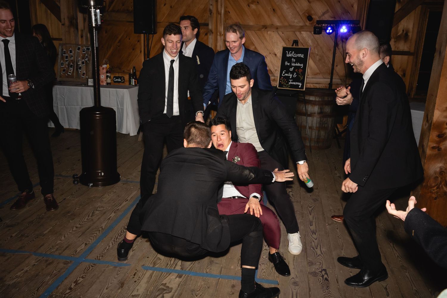 Guests dancing and having fun at a wedding reception in a rustic wooden barn venue with ambient lighting.
