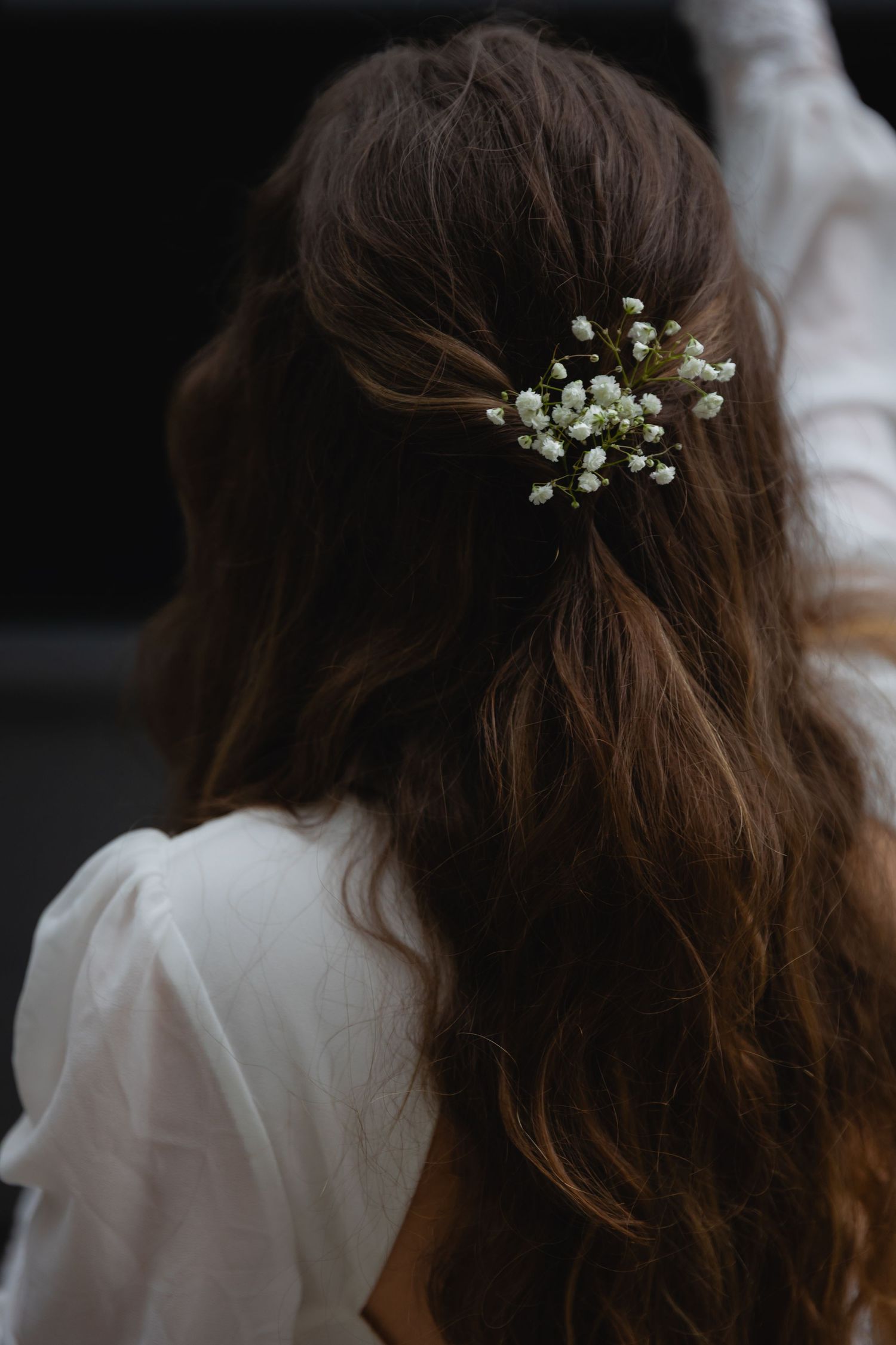 Small white flowers delicately placed in wavy brown hair against a dark background.