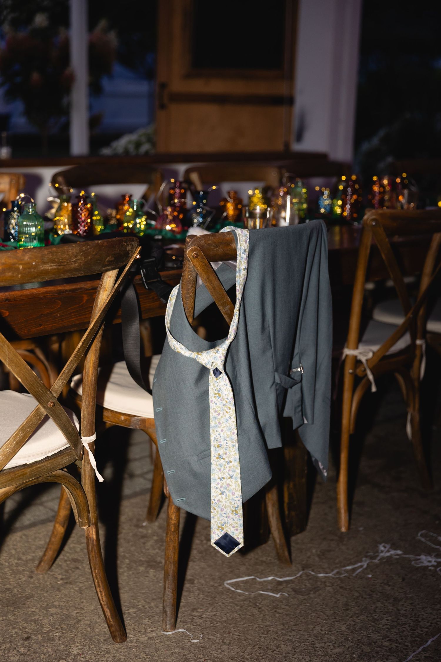 Gray and white neckties hang decoratively from rustic wooden chairs at an evening wedding reception.