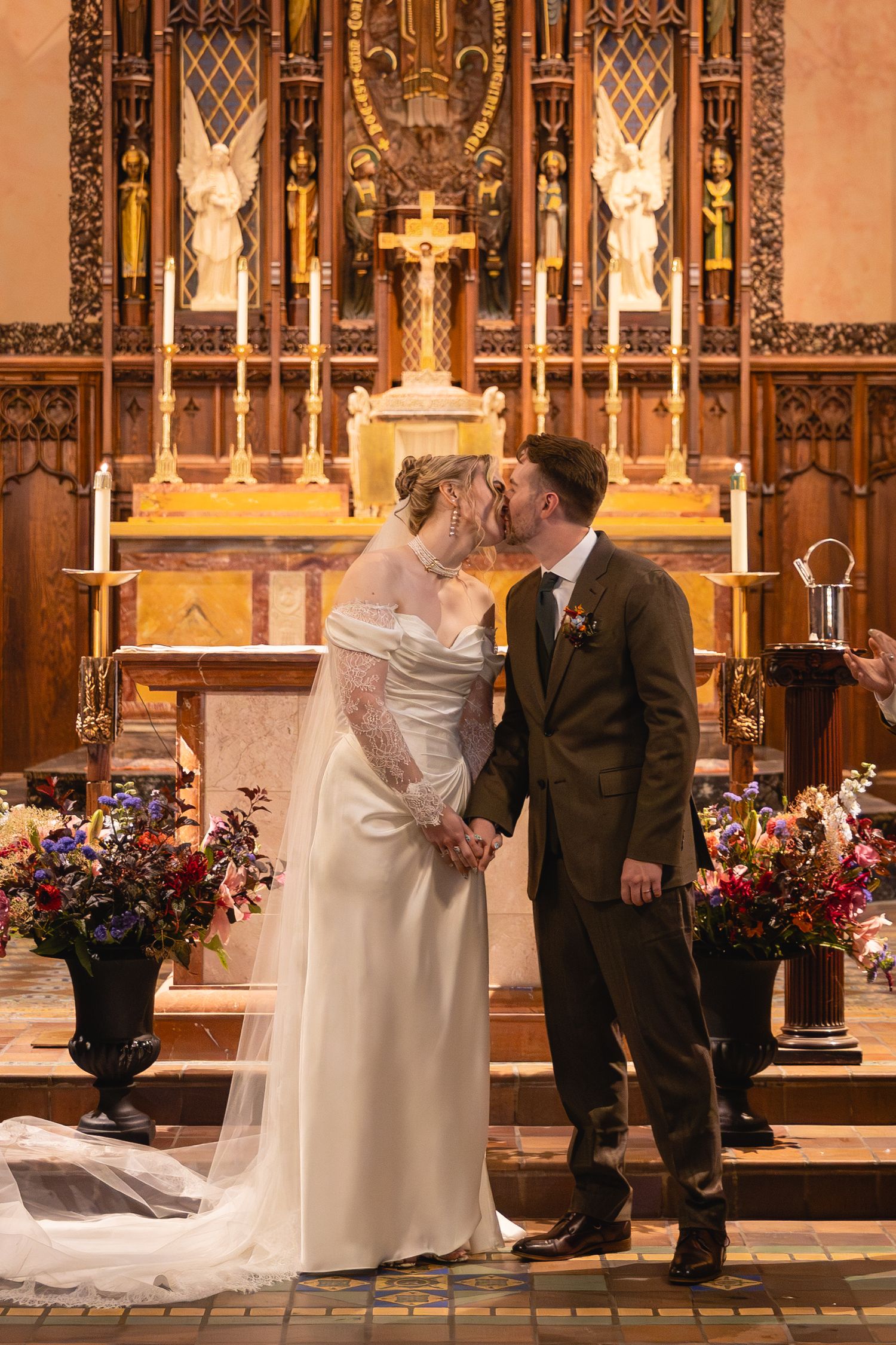 A wedding ceremony in a church with ornate stained glass windows and floral arrangements at the altar.