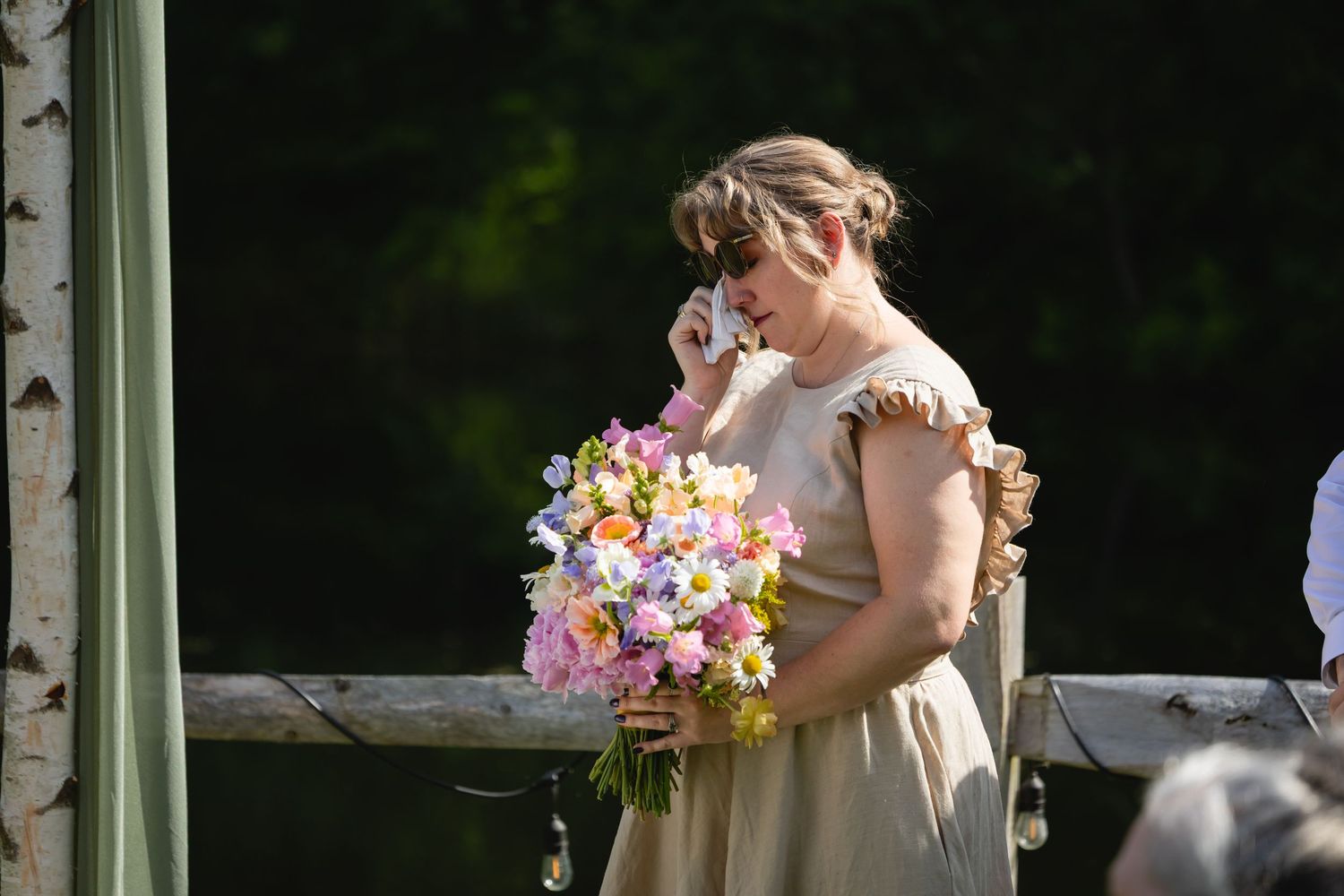 A bride and groom share their first kiss during an outdoor wedding ceremony under a floral-adorned arch.