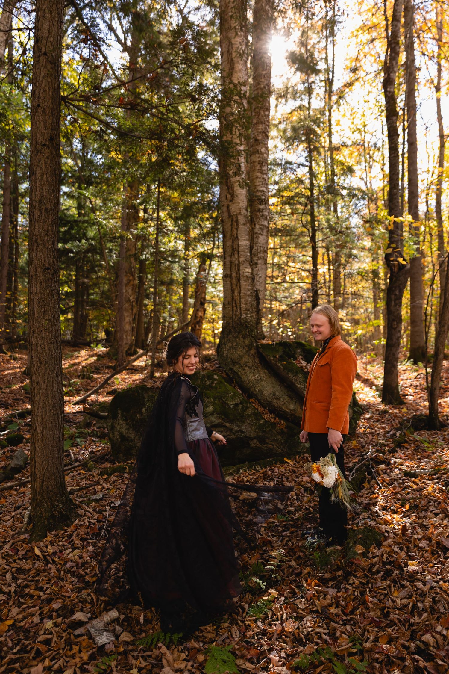 Group of people sitting among fallen autumn leaves in a sunlit forest during golden hour.