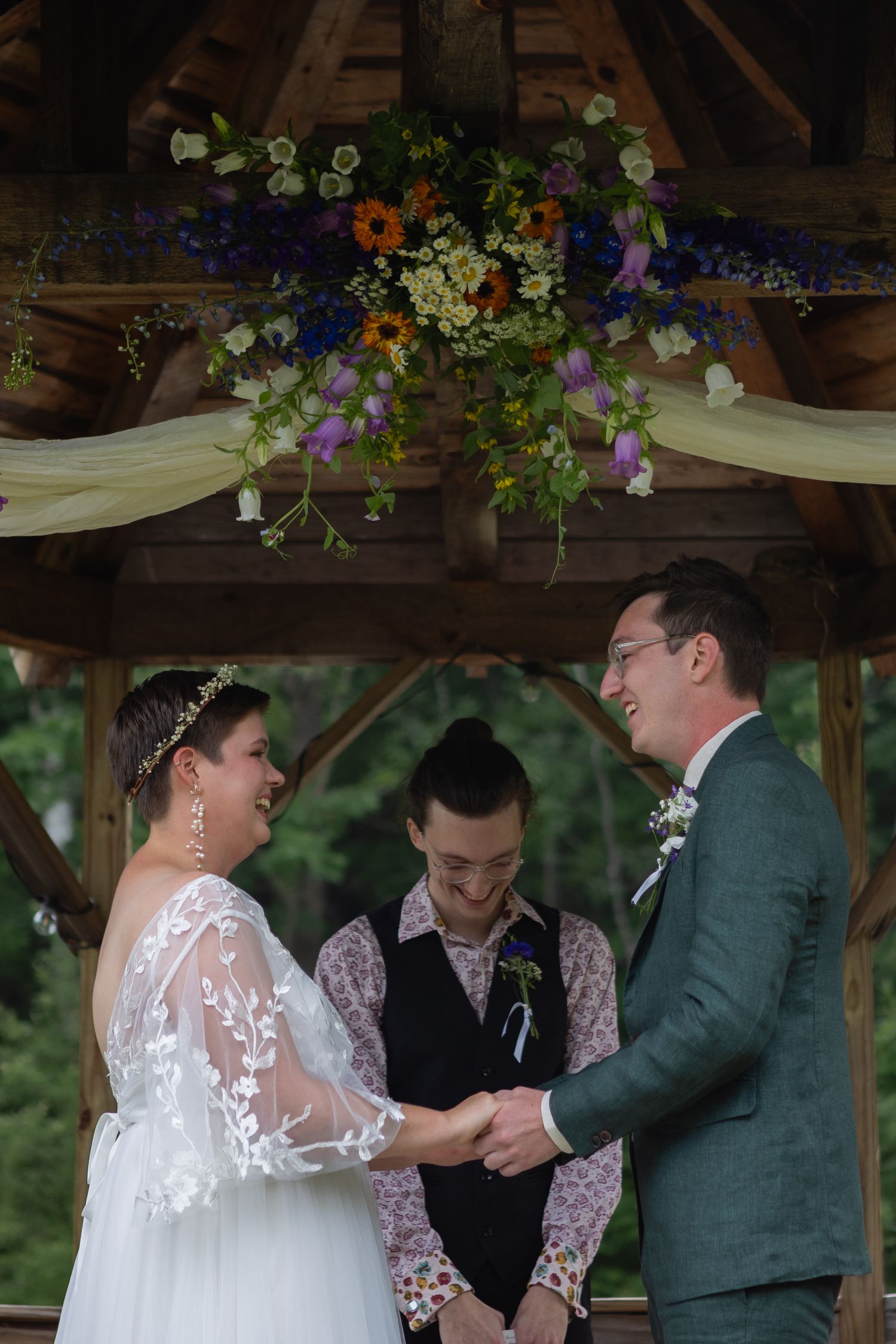 Intimate wedding ceremony moment under a rustic gazebo decorated with wildflowers and white fabric.