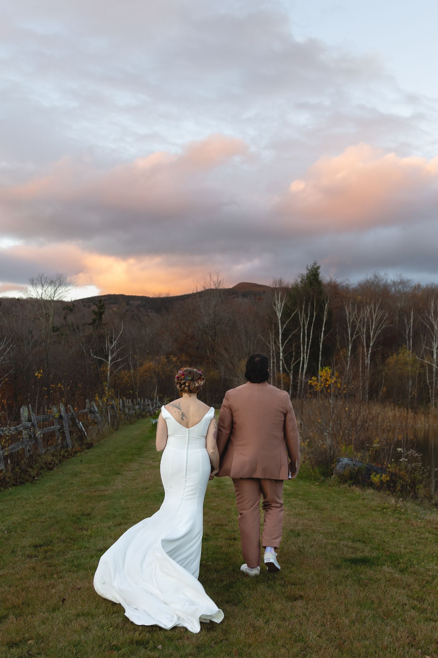 Wedding couple walks away into sunset with dress train flowing behind.