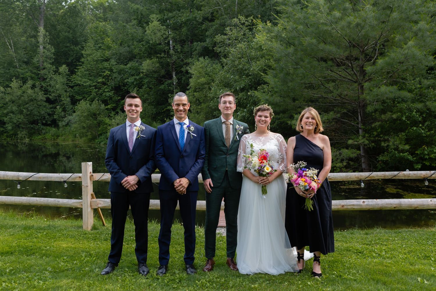 Wedding party poses for formal photo by rustic fence in garden setting.