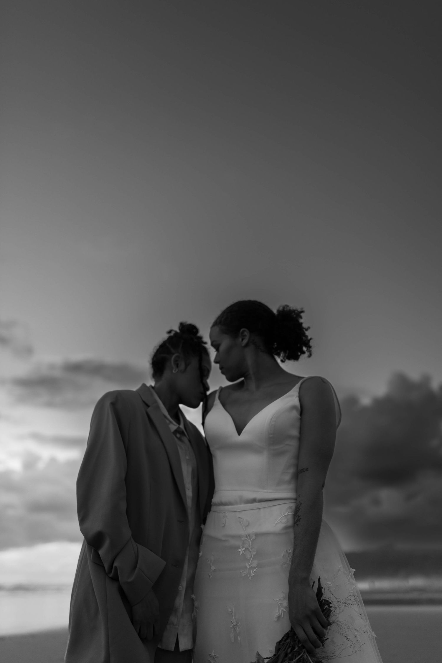 An intimate black and white portrait of a couple sharing a romantic moment at sunset.