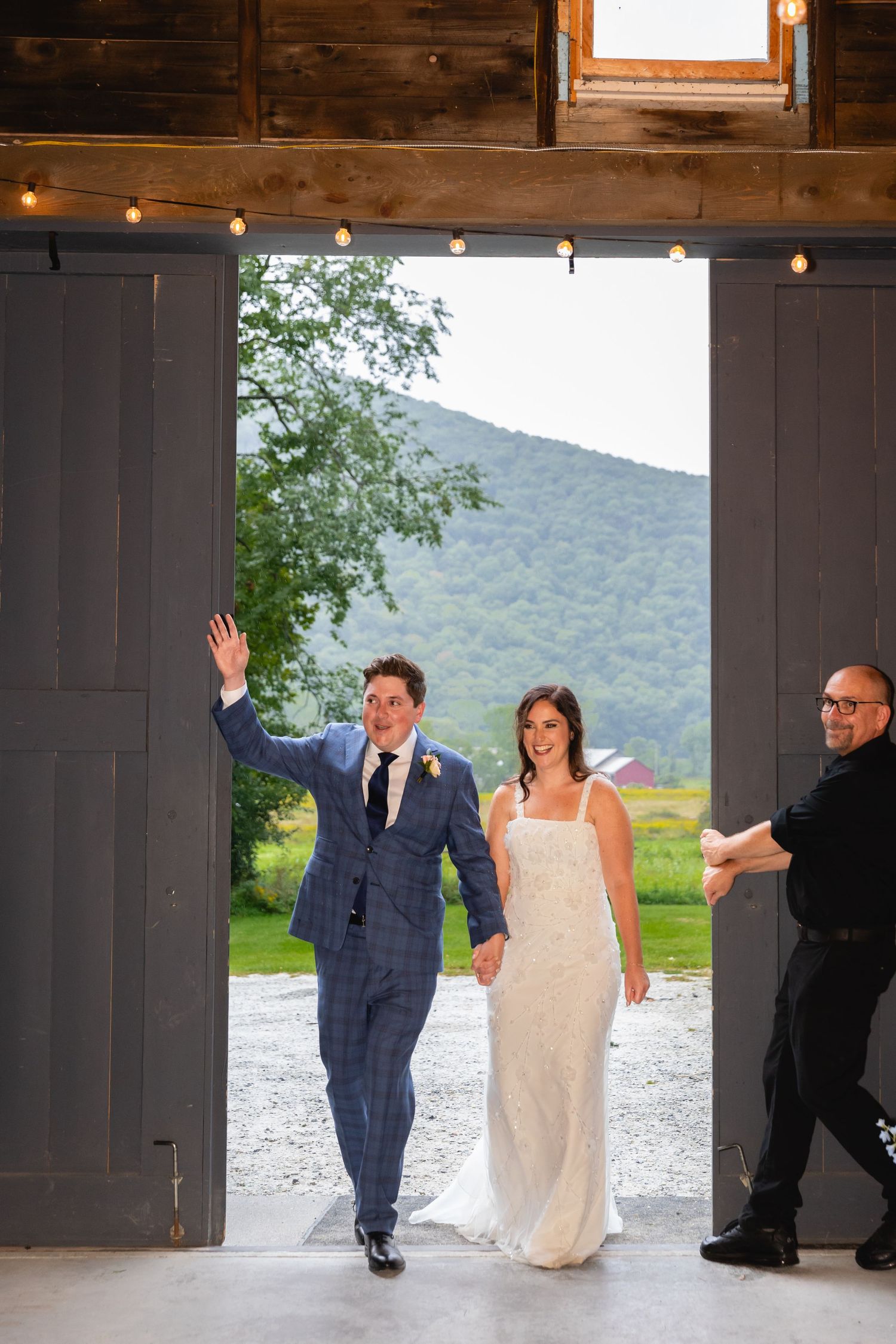 A couple makes their grand entrance through rustic barn doors with mountain views and string lights overhead.