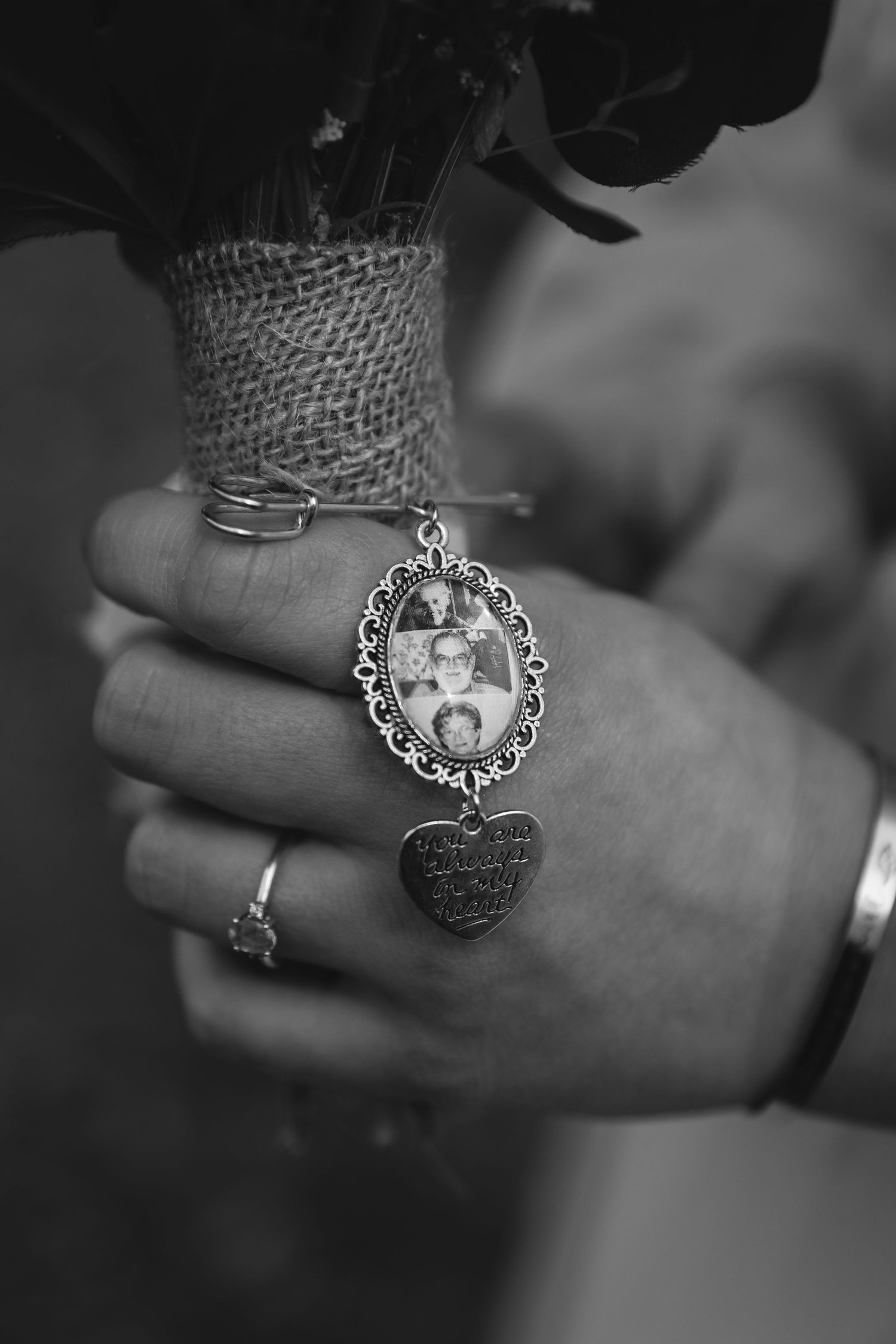 Close-up of hand wearing rings with vintage photo locket charm in black and white.