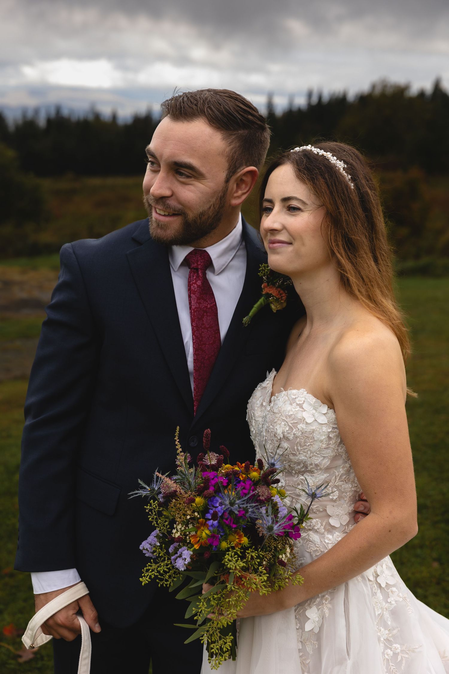 A couple shares a tender moment in formal wedding attire with a colorful wildflower bouquet.