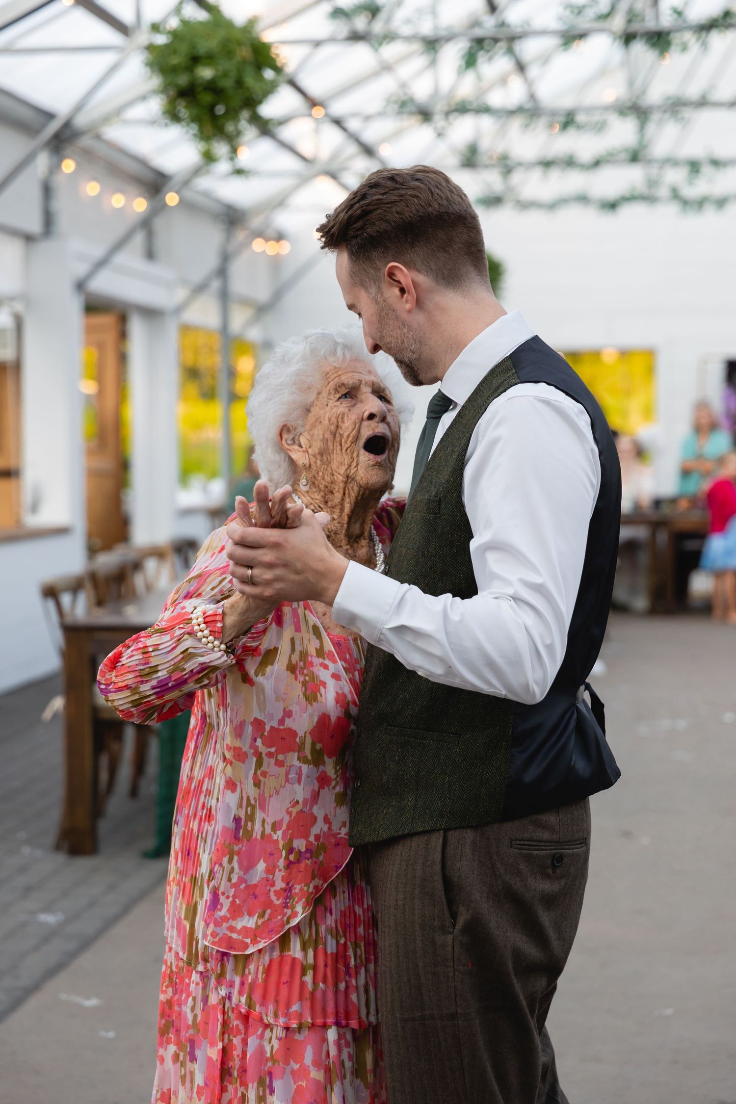 A couple dancing together in a greenhouse venue with romantic lighting and floral decor.