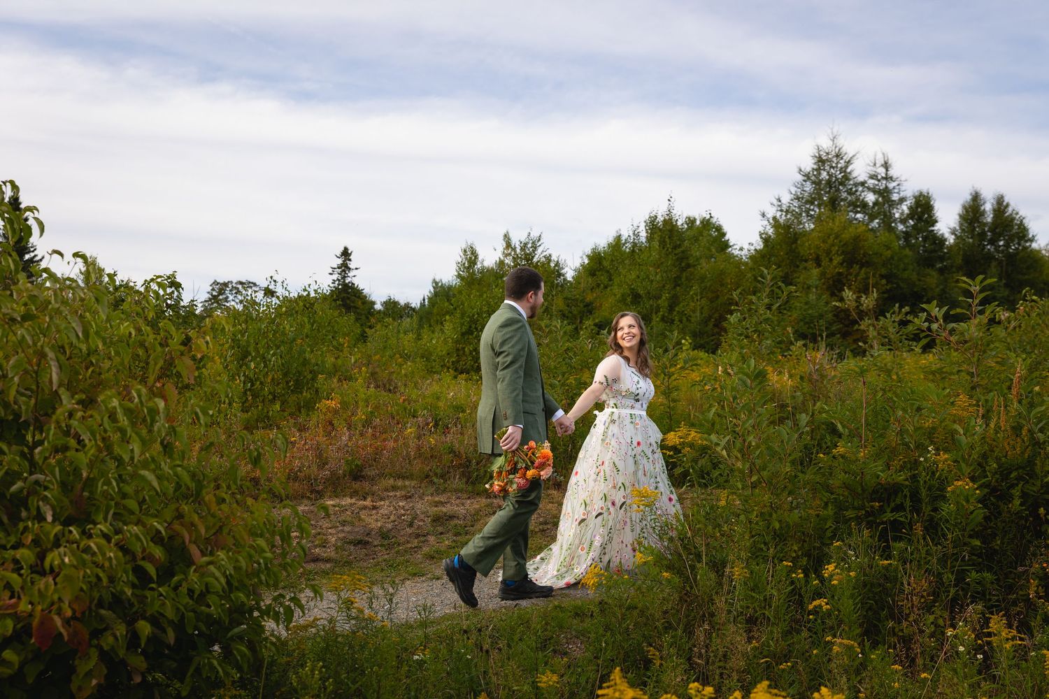 A couple walks through a scenic natural landscape during a golden sunset photo session.