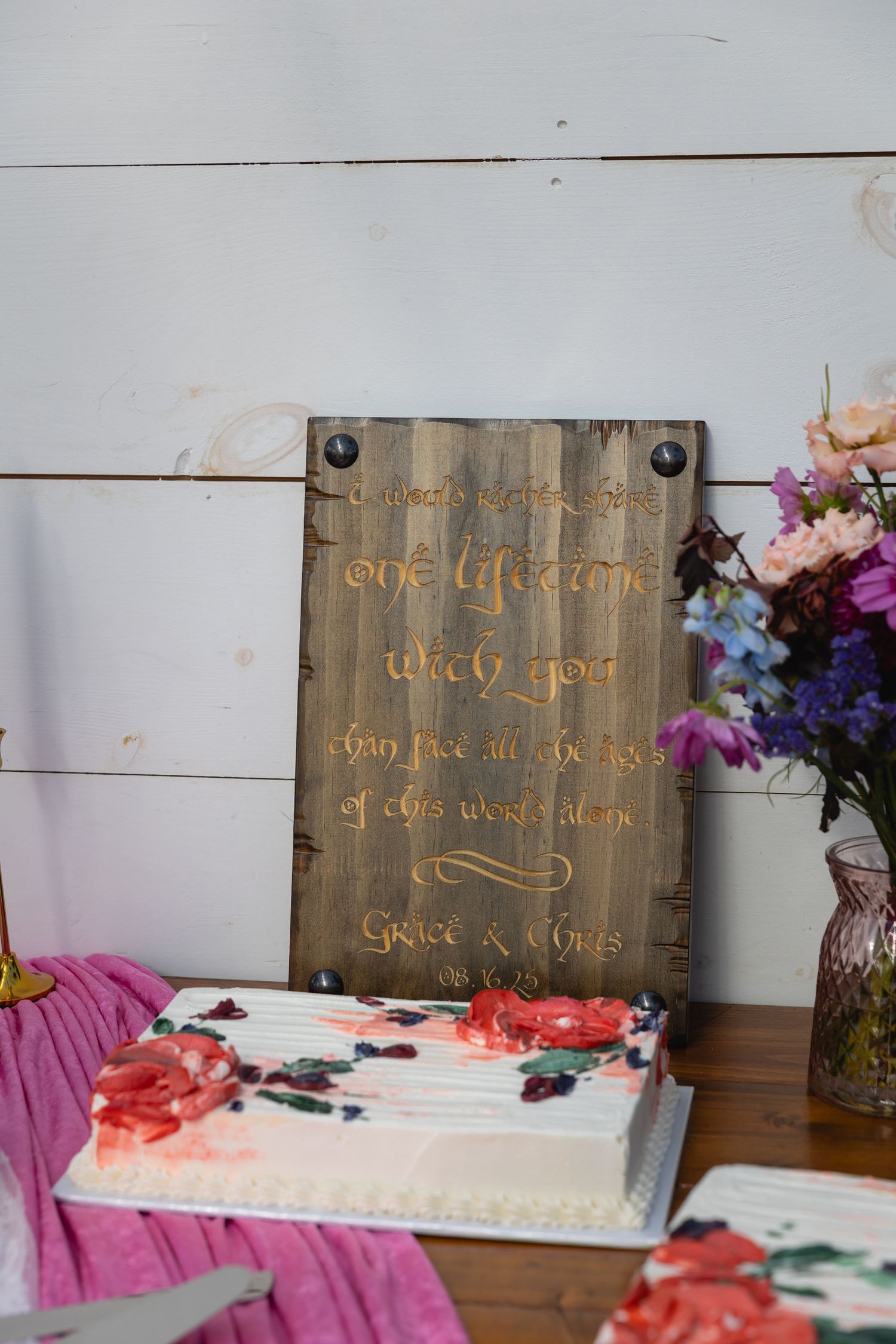 Rustic wooden signs with decorative text displayed alongside colorful floral arrangements and pink fabric accents.