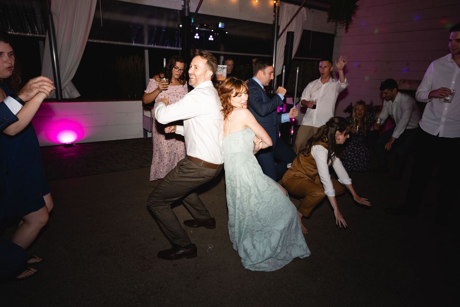 People dancing and celebrating at a dimly lit party or reception venue with festive lighting and atmosphere.