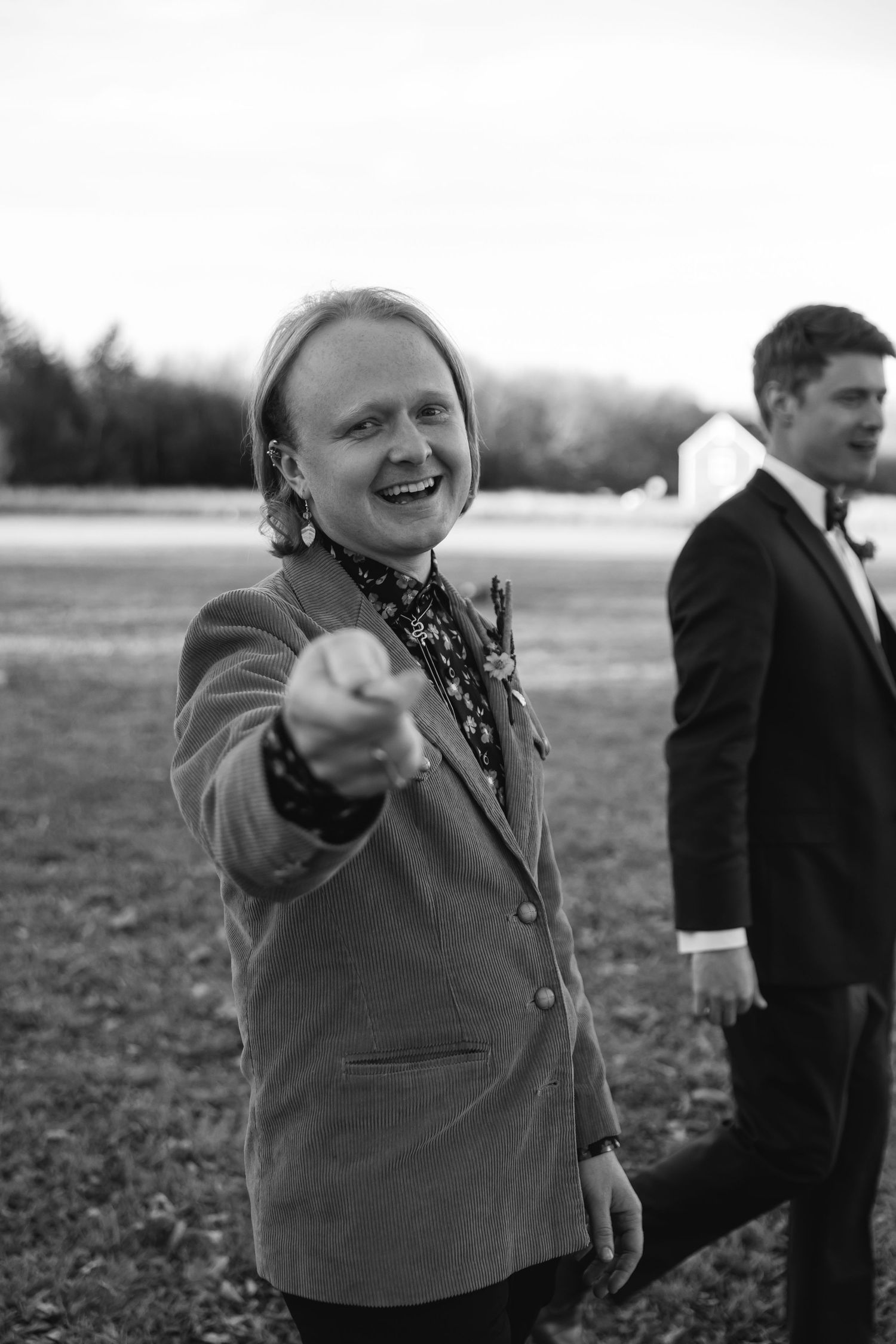 A group of people in vintage attire point and gesture animatedly in a black and white outdoor scene.