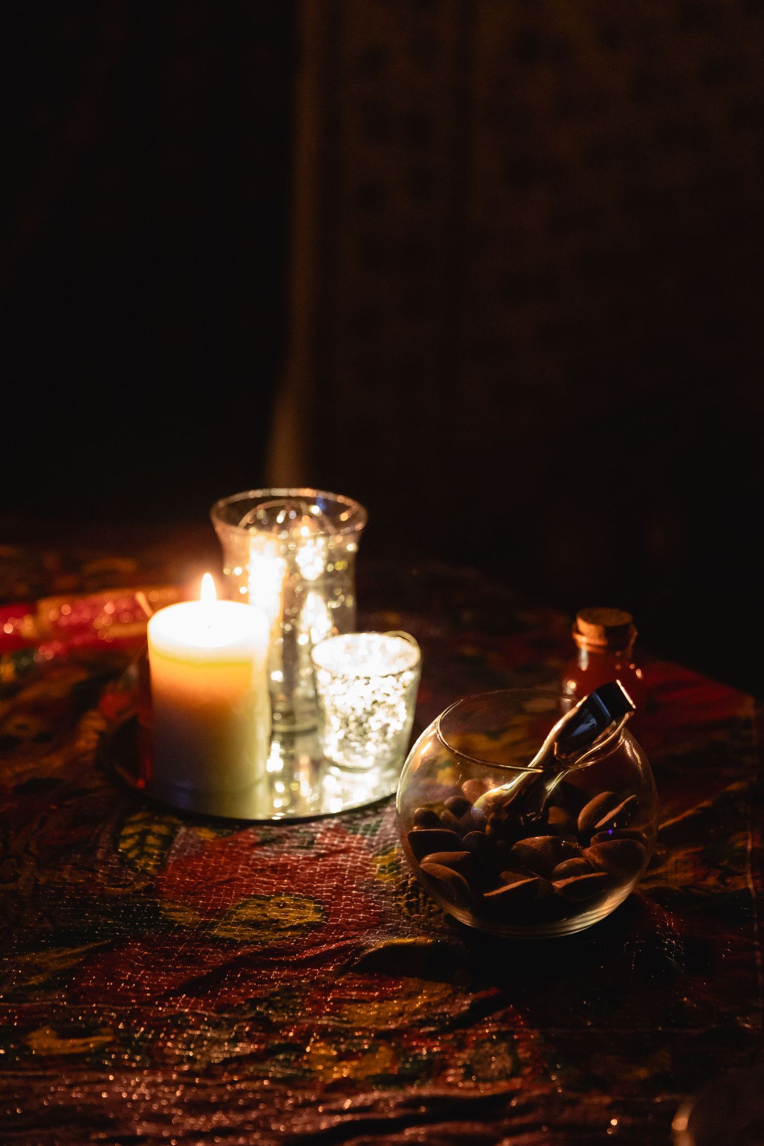Romantic candlelit table display with glowing candle, fairy lights, and glass bottle on decorative fabric.