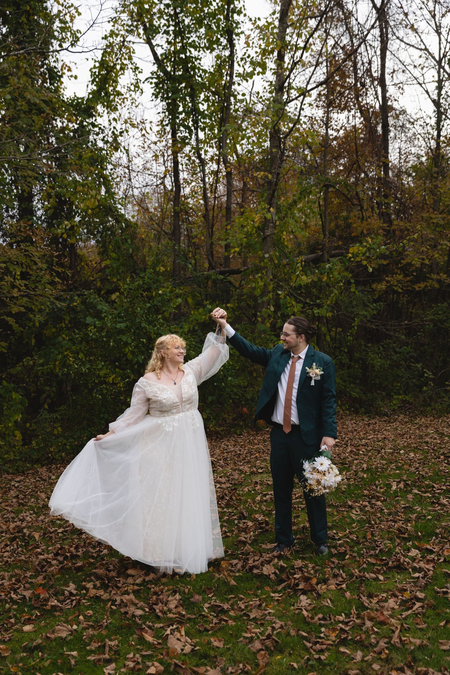 A couple dancing together outdoors among fallen autumn leaves.