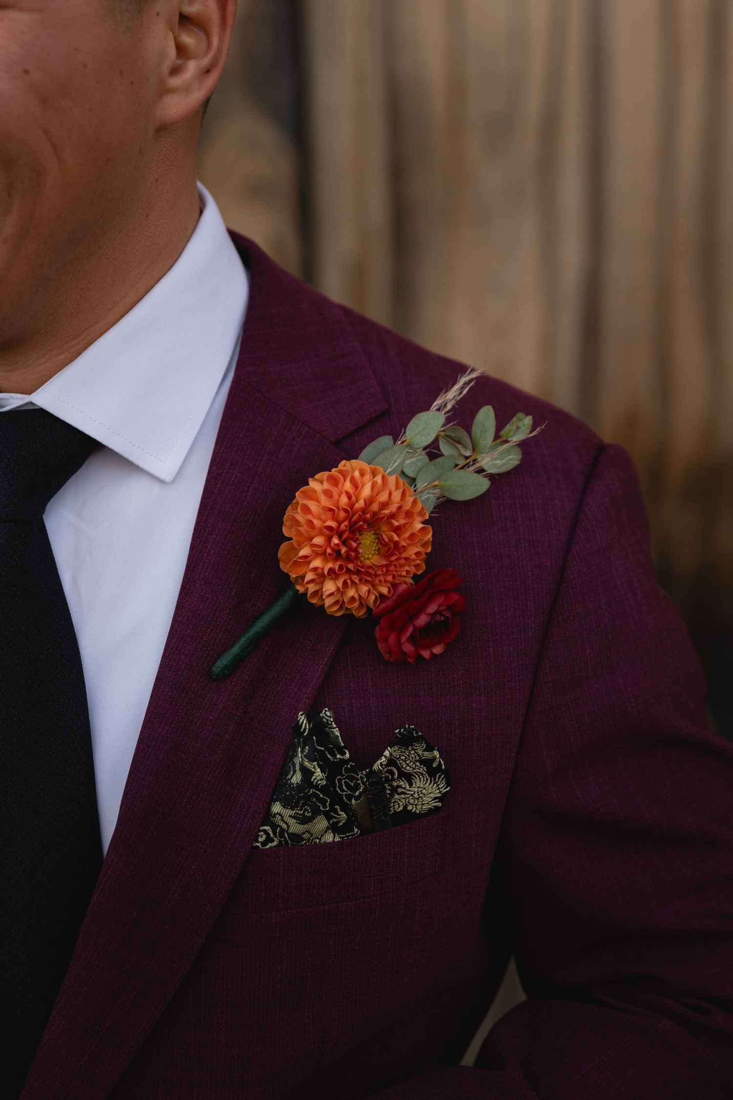 Close-up of a burgundy suit jacket with an orange dahlia boutonniere and patterned pocket square.