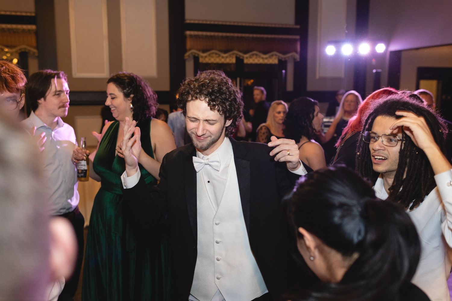 Celebratory dancers in formal attire enjoying themselves on a dance floor with purple lighting in the background.