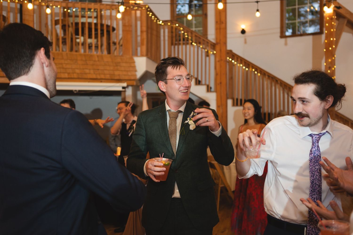 Wedding reception guests dancing and celebrating in a rustic wooden venue with string lights.