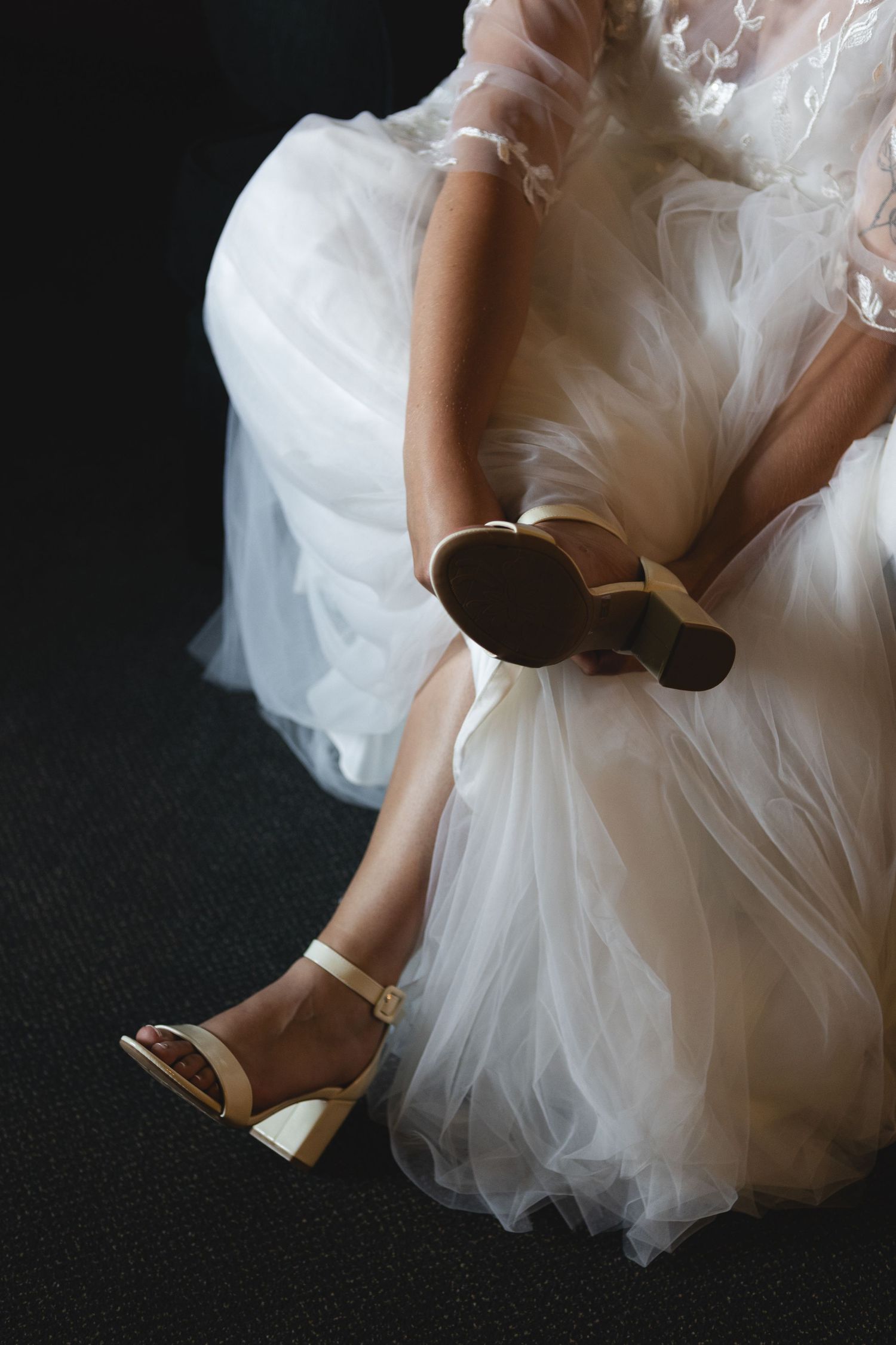 White wedding dress fabric and gold heeled shoes against dark background.