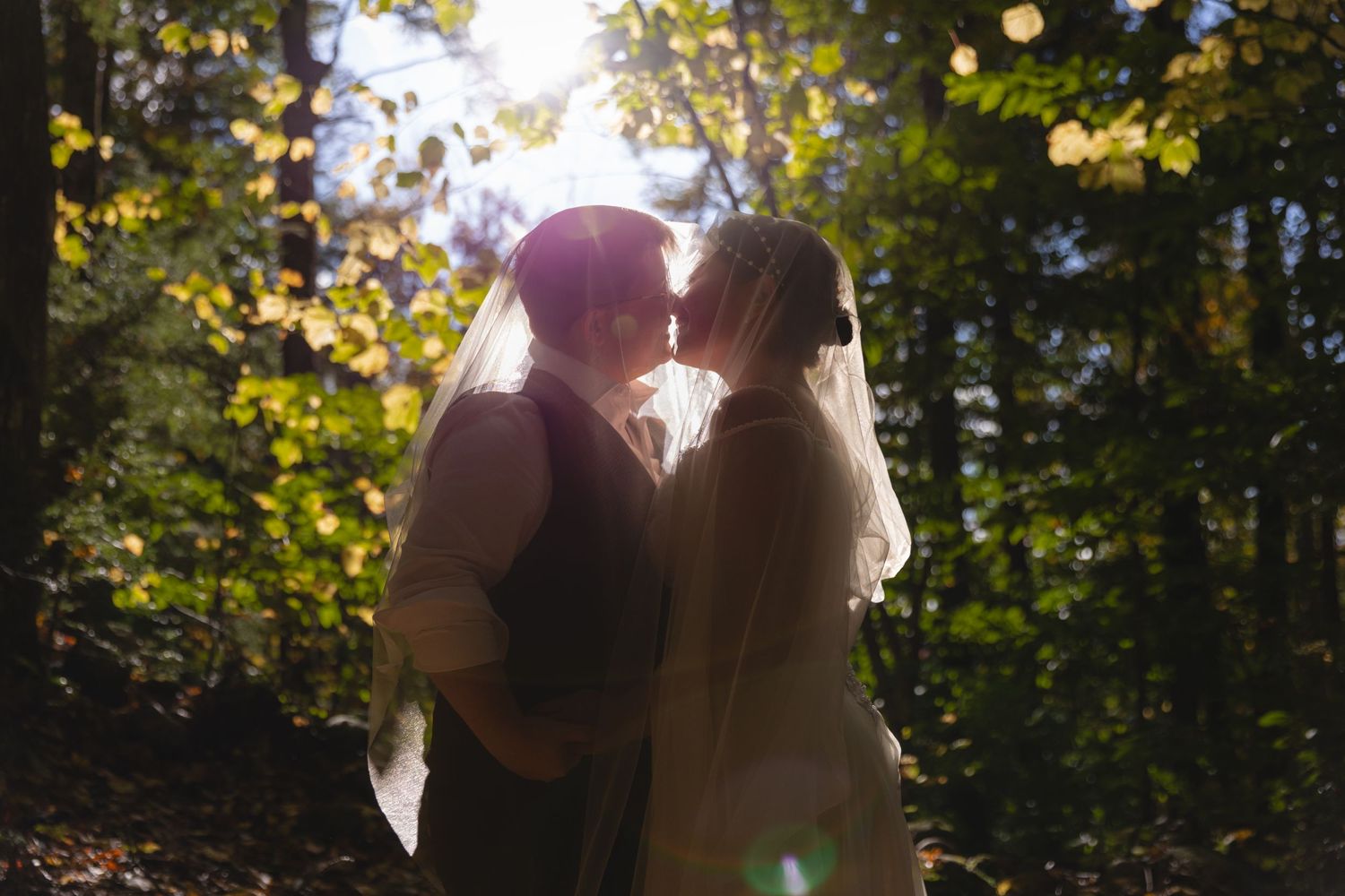 Silhouette of a wedding couple embracing in a sunlit autumn forest.