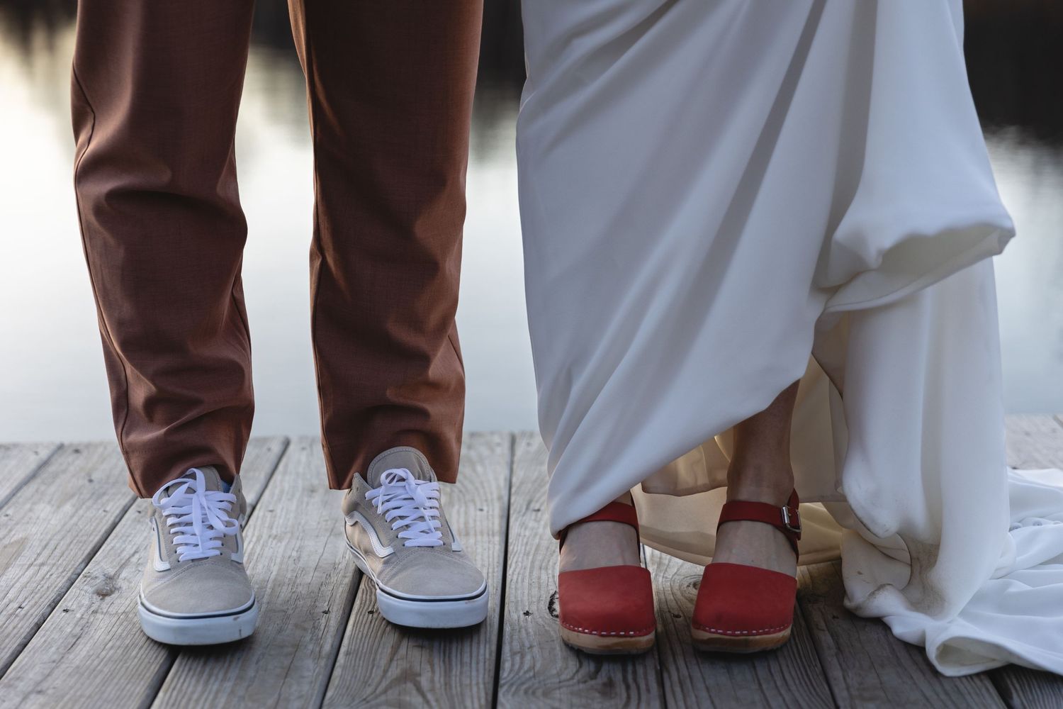 Contrasting footwear choices of wedding couple showing casual sneakers and formal shoes on wooden deck.