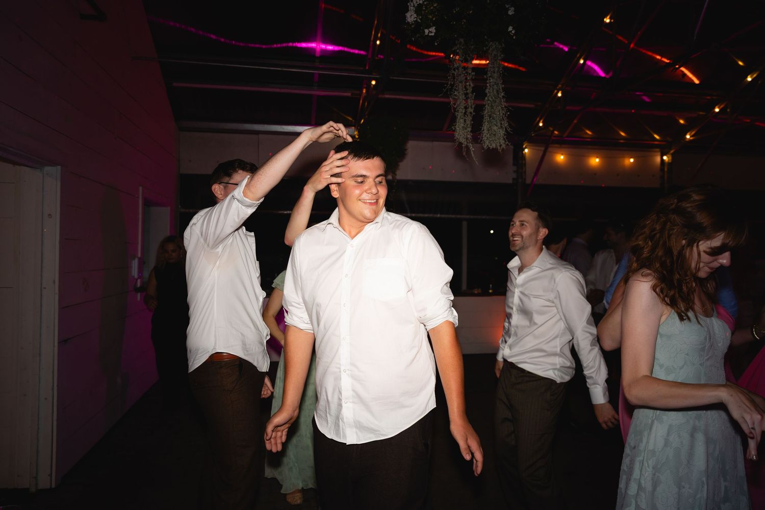 People dancing and socializing at a dimly lit party venue with pink and purple lighting effects.
