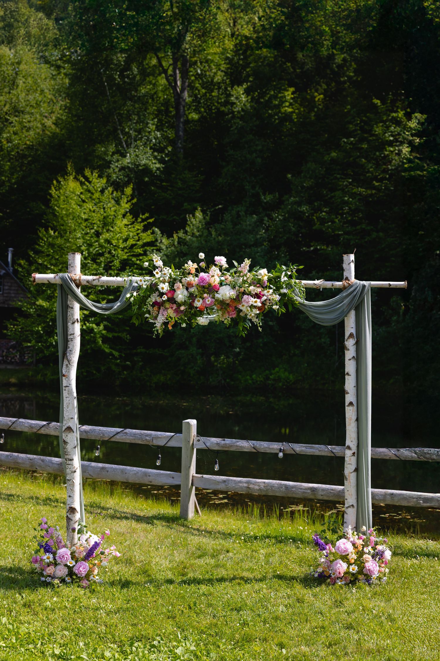 Rustic wooden fence posts decorated with elegant floral arrangements and white fabric draping in an outdoor garden setting.